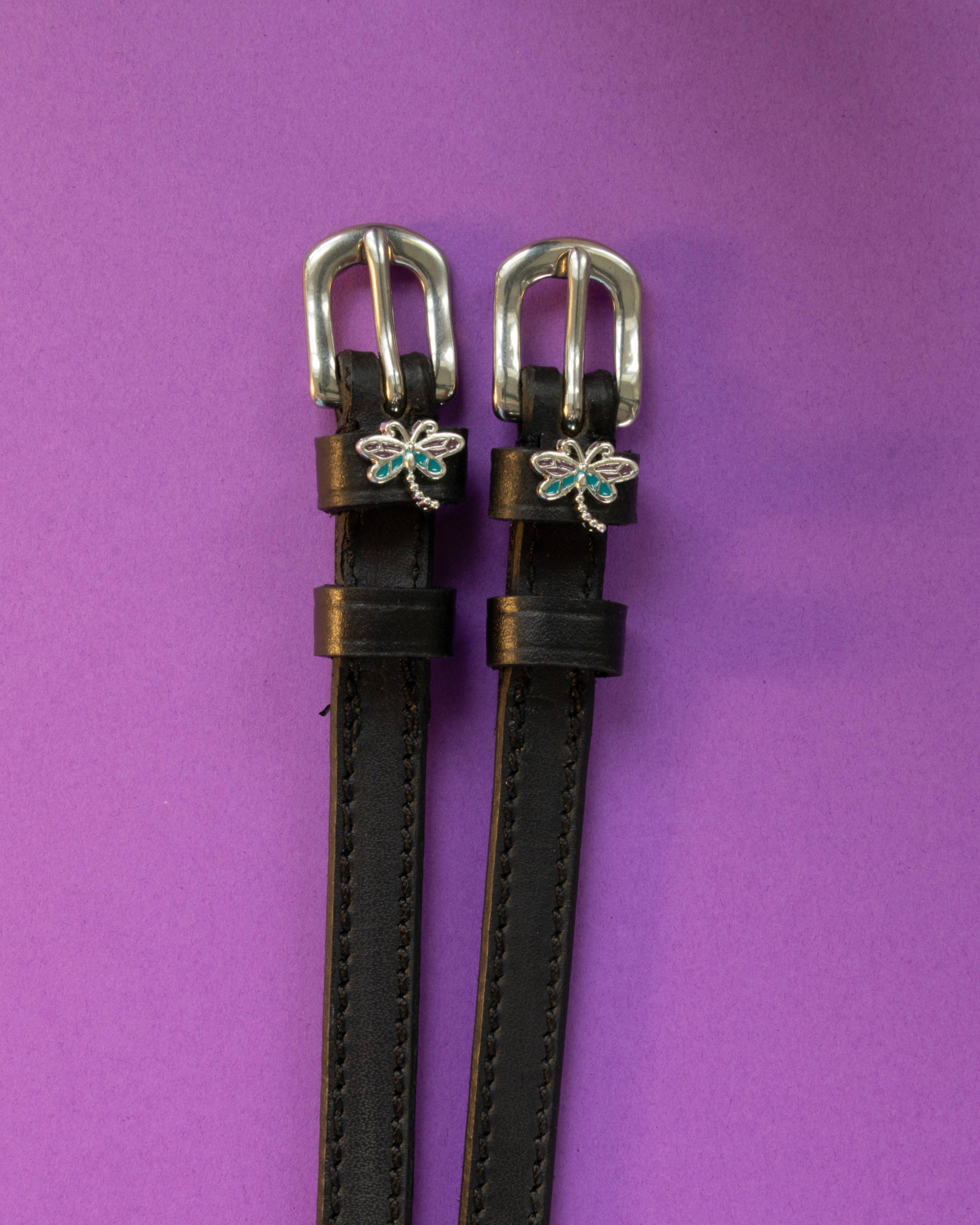 Dragonfly ManeJane spur straps with the signature Dragonfly charm, shown on a purple background