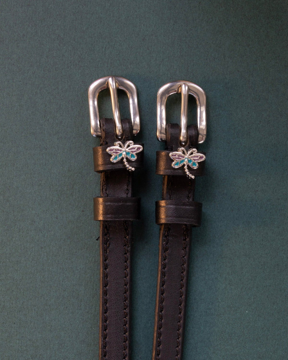 Dragonfly ManeJane spur straps with the signature Dragonfly charm, shown on a charcoal background