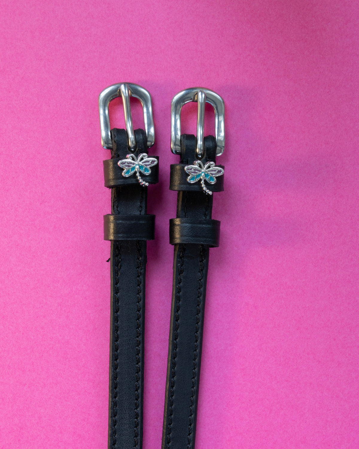 Pair of Dragonfly ManeJane spur straps, black leather with stainless buckles, on a magenta backdrop