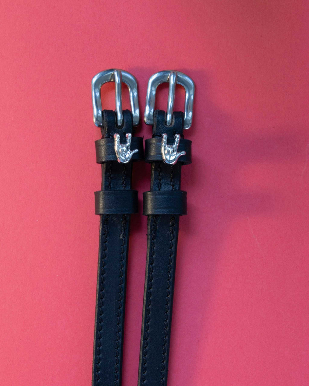 Pair of Rock On ManeJane spur straps, black leather with stainless buckles, on a coral backdrop