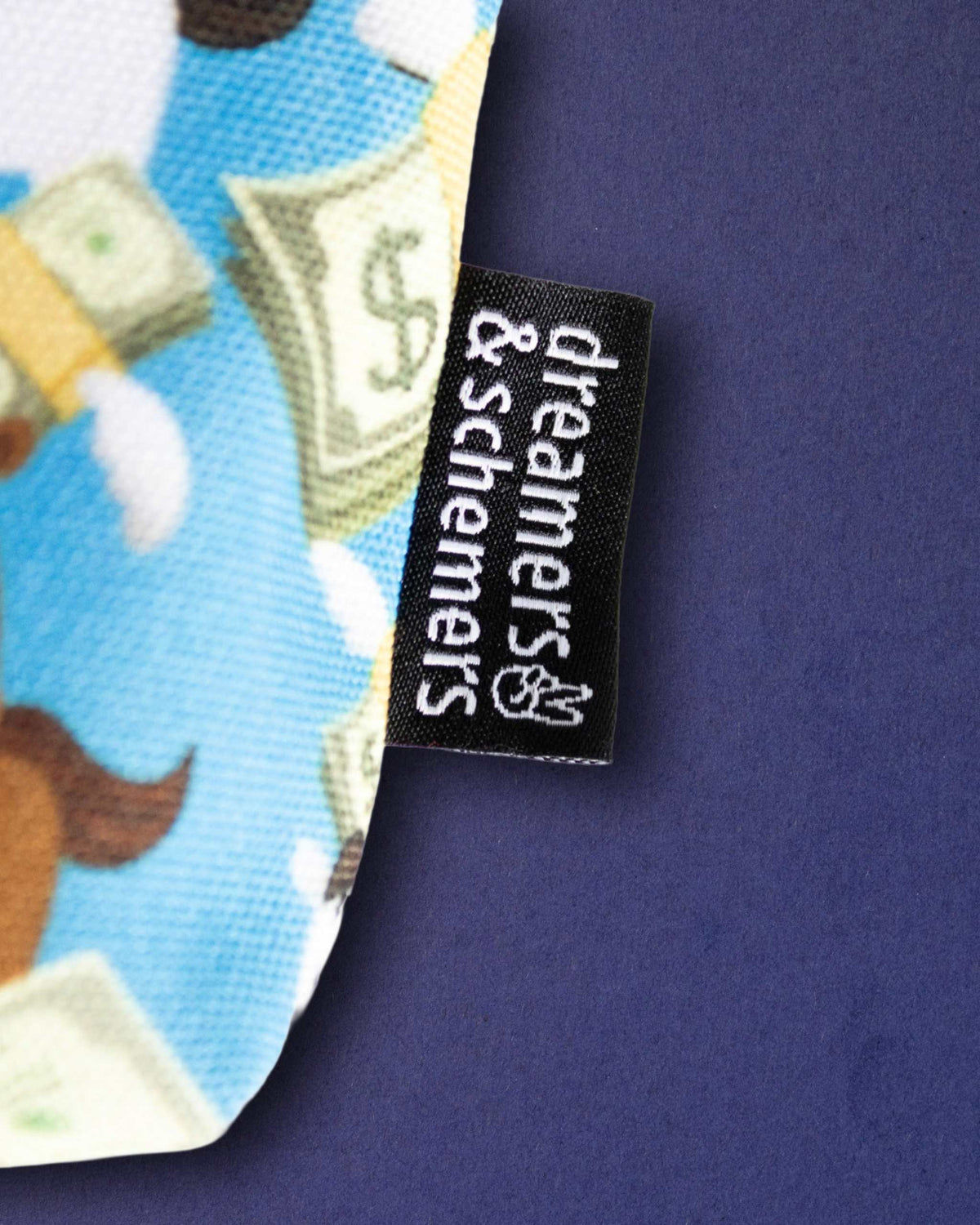 Woven dreamers & schemers label at the seam of the Cash Money pouch, dollar-bill print behind