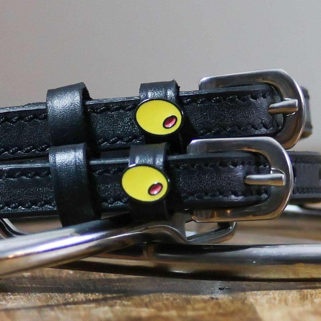 Black leather Spur Straps with stainless steel buckles and custom yellow charm close-up