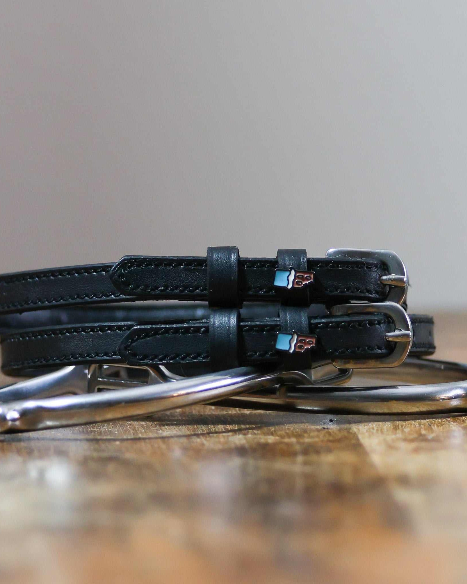 Black leather Chocolate Bar Spur Straps with stainless steel buckles and custom charm on wooden surface