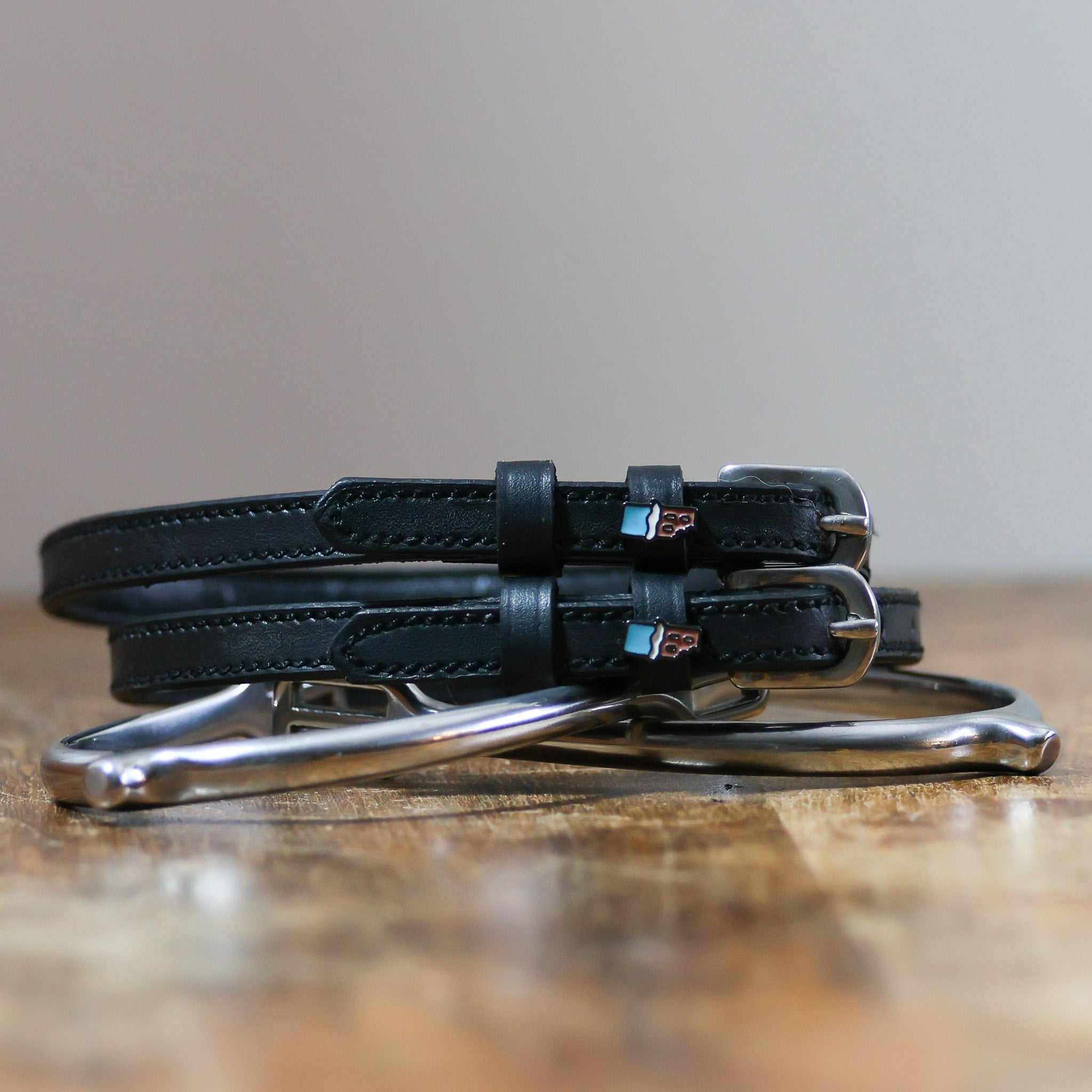 Black leather Chocolate Bar Spur Straps with stainless steel buckles and custom charm on wooden surface