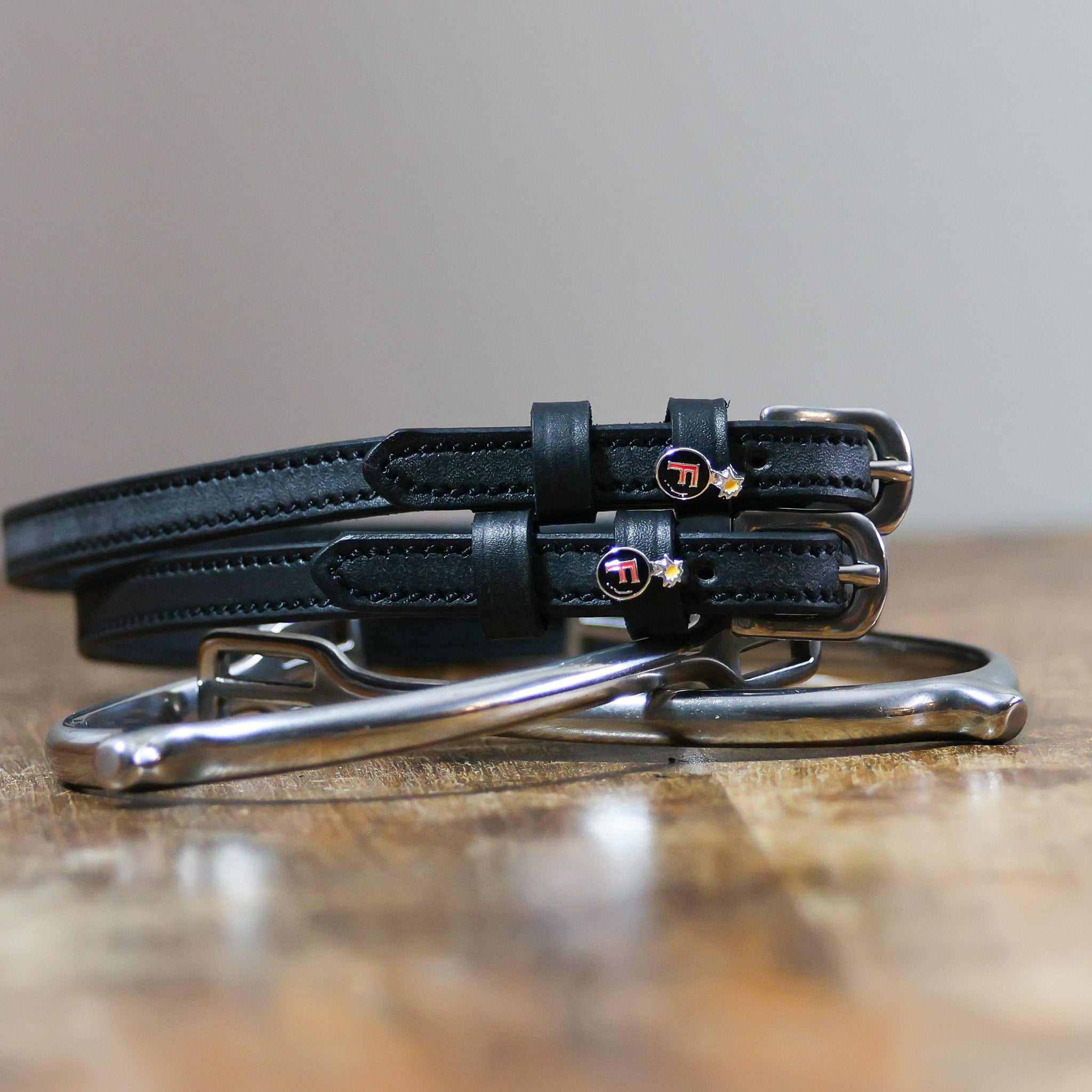 Black leather F Bomb Spur Straps with stainless steel buckles and custom charms on wooden surface