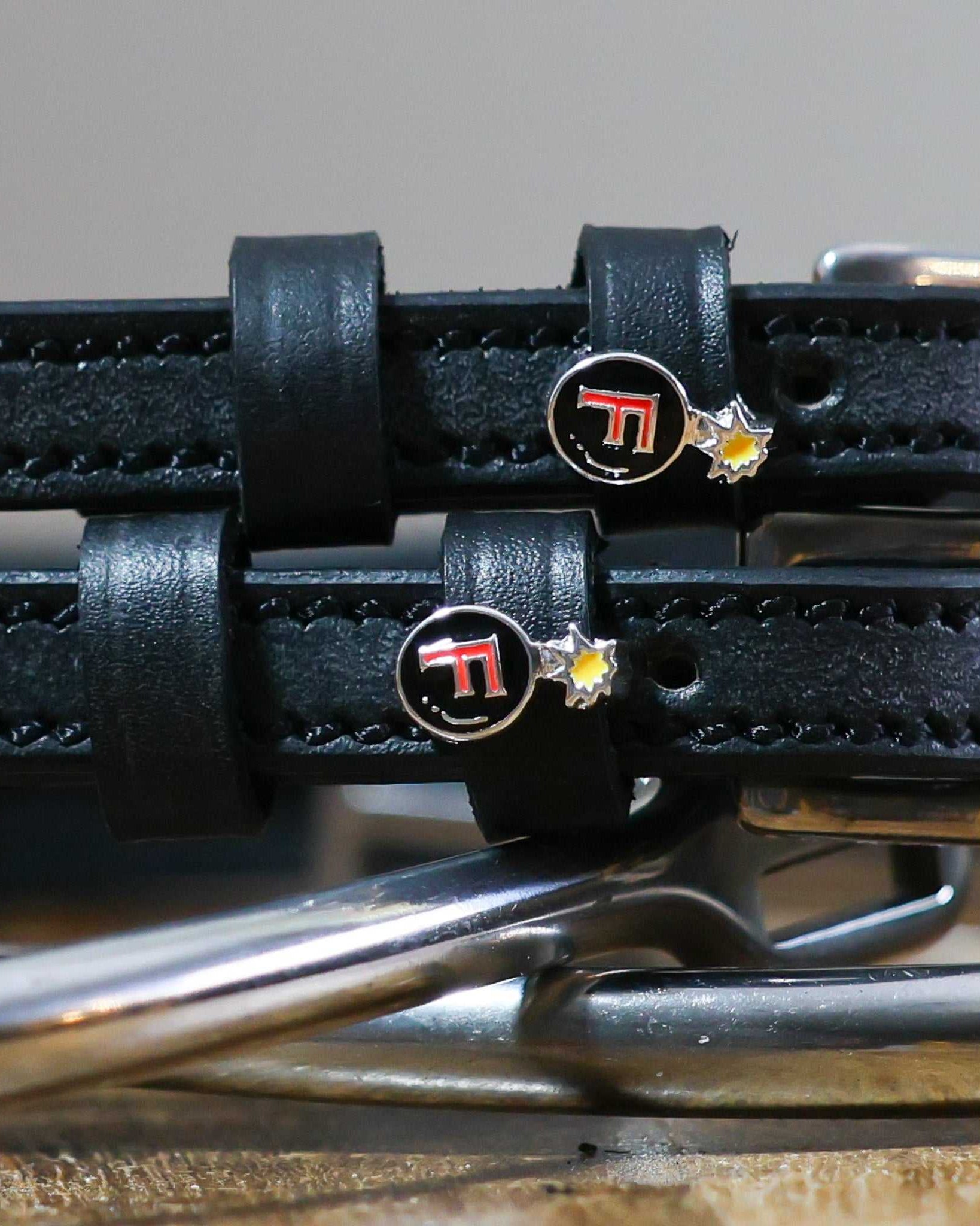 Close-up of black leather spur straps with metal buckles featuring F-Bomb design pins from Ultimate F-Bomb Pack equestrian accessories.