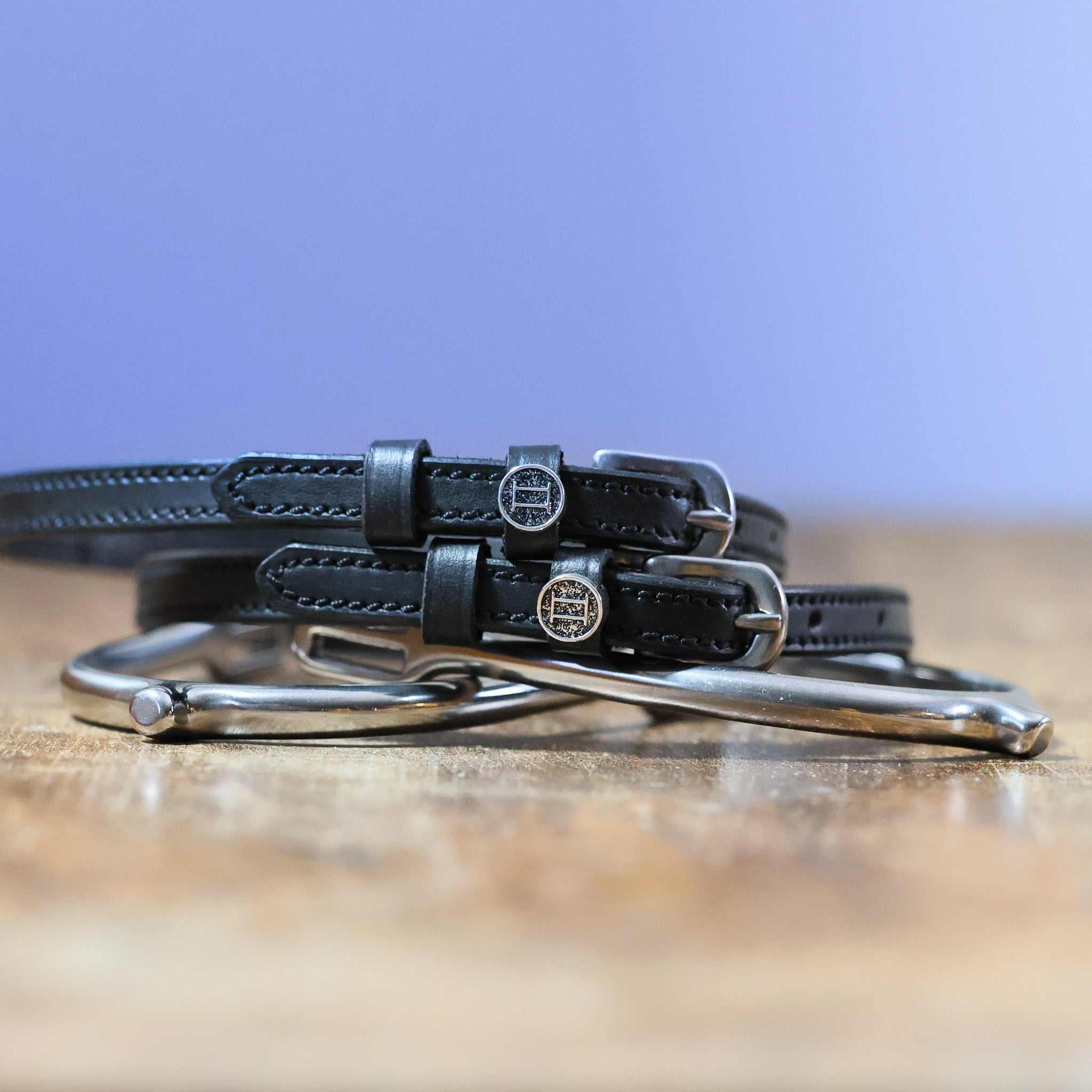 Black leather Gemini Spur Straps with stainless steel buckles and custom charms on wooden surface