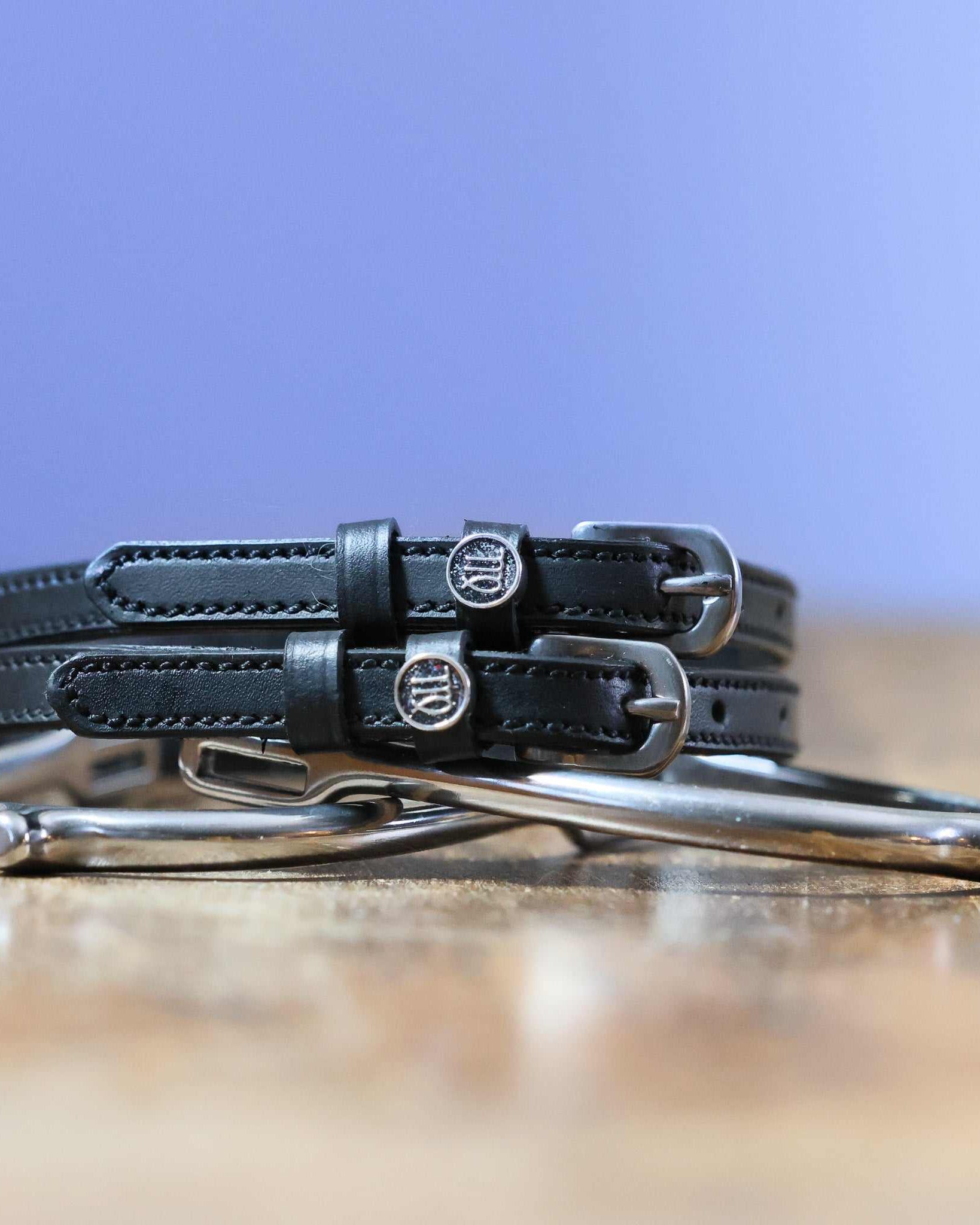 Virgo Spur Straps black leather with stainless steel buckles and custom charm on wooden surface