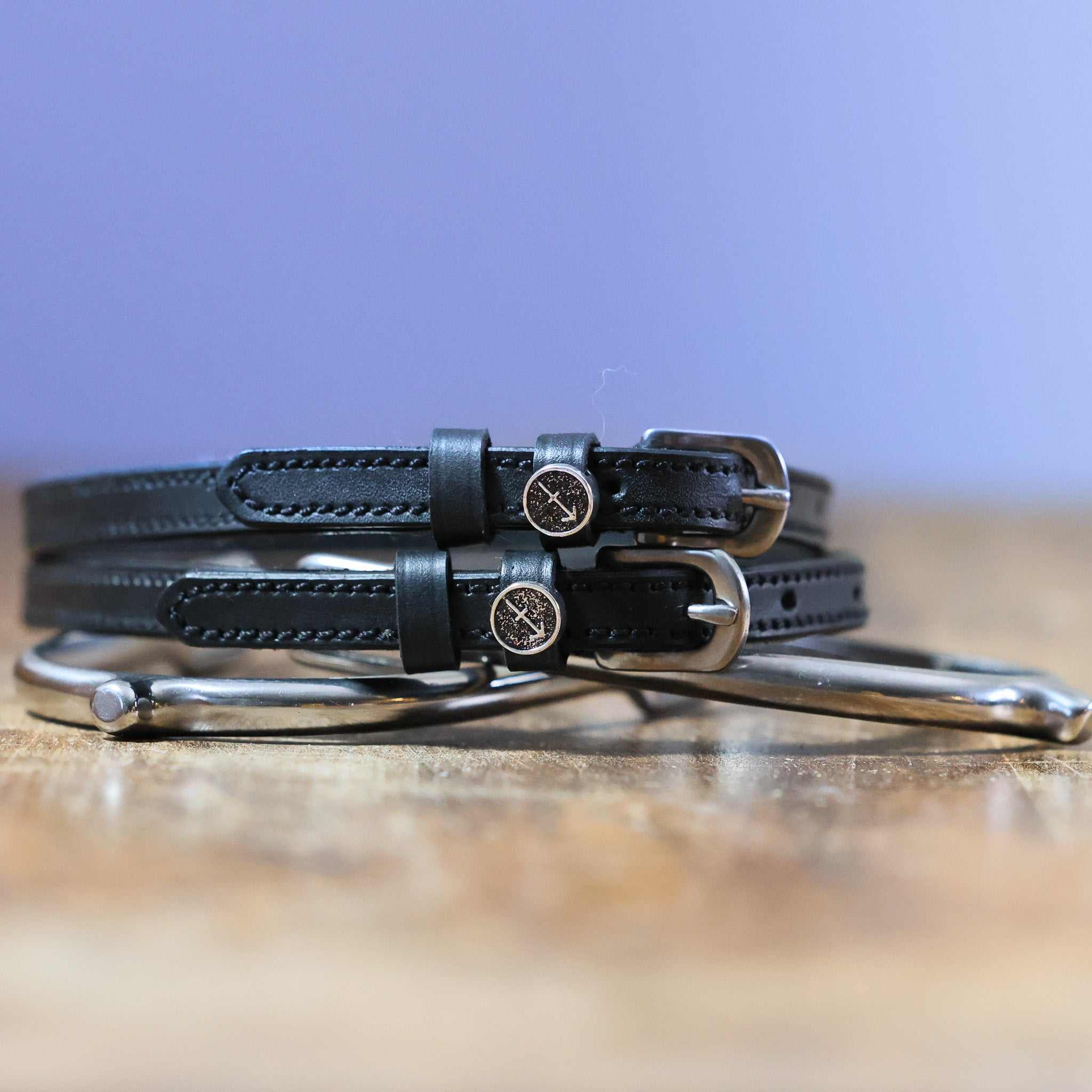 Black leather Sagittarius Spur Straps with stainless steel buckles and custom charm on wooden surface