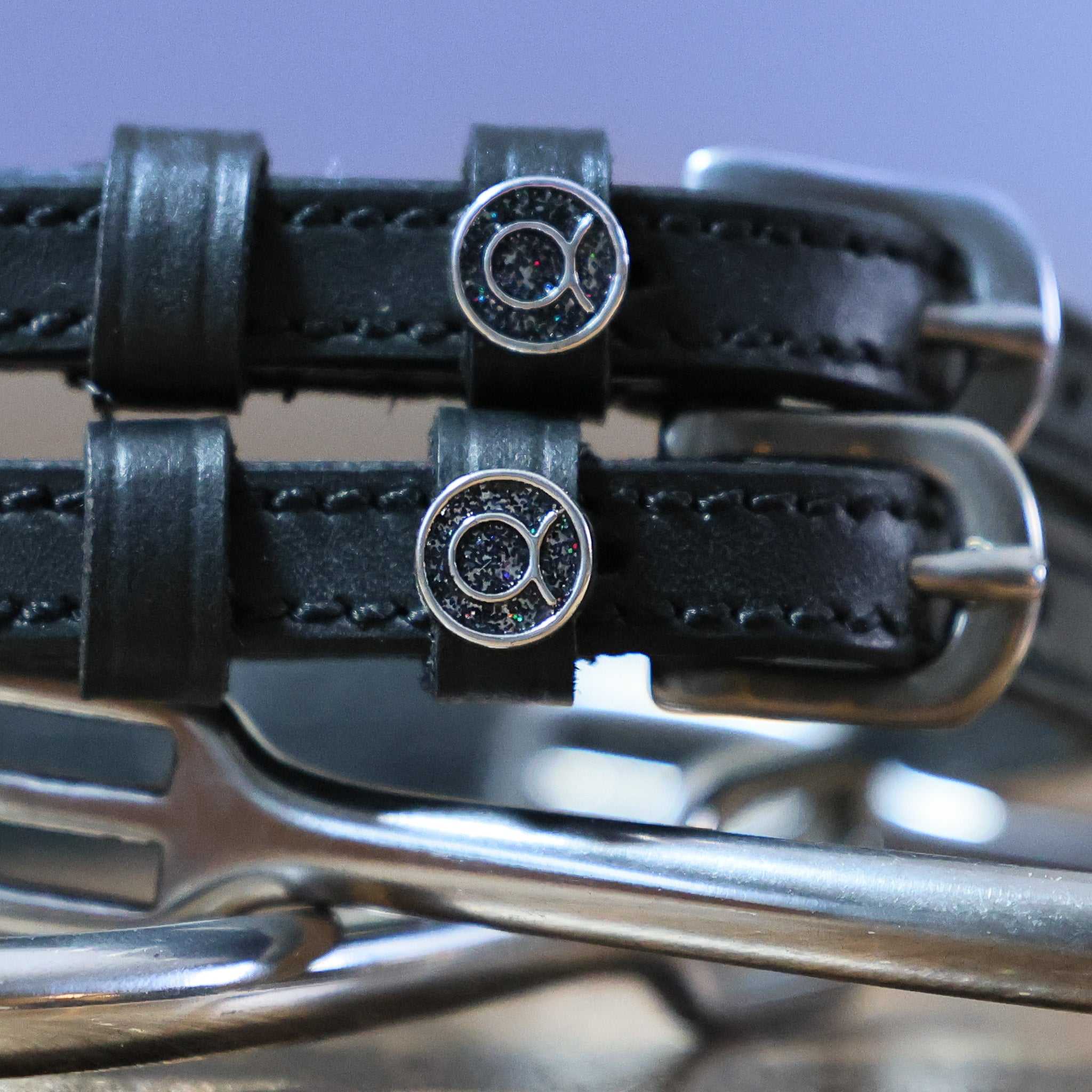 Close-up of black leather Taurus Spur Straps with stainless steel buckles and custom charm on metal spurs