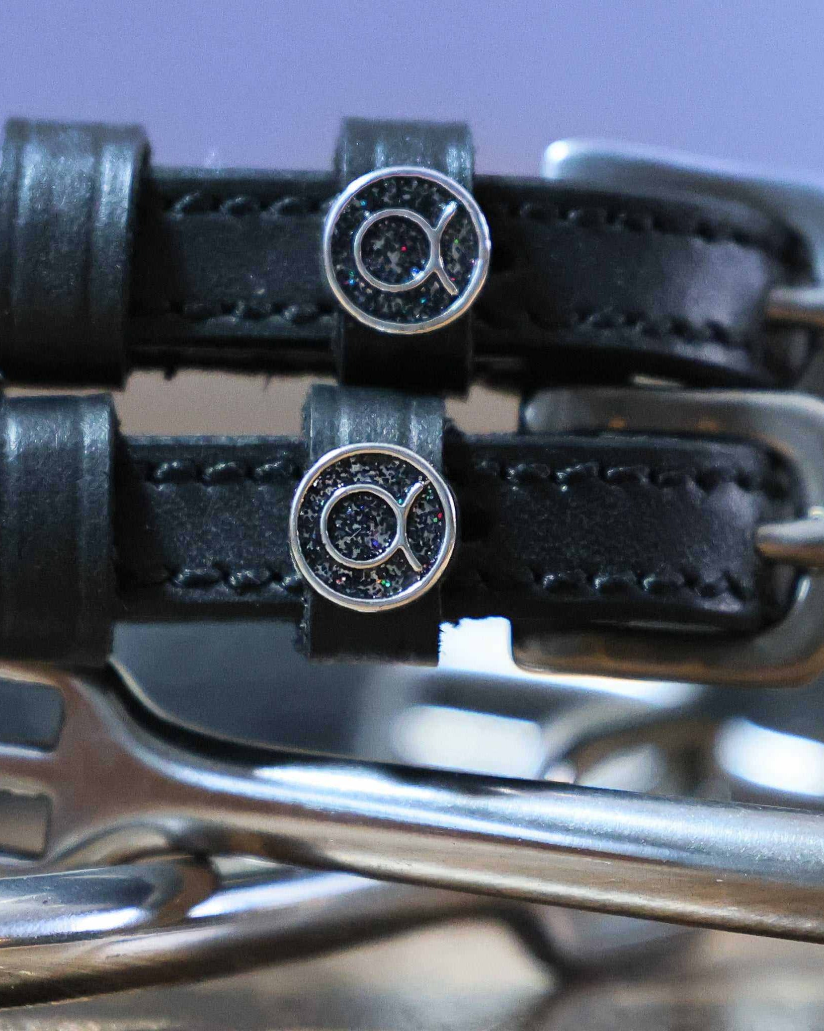 Close-up of black leather Taurus Spur Straps with stainless steel buckles and custom charm on metal spurs