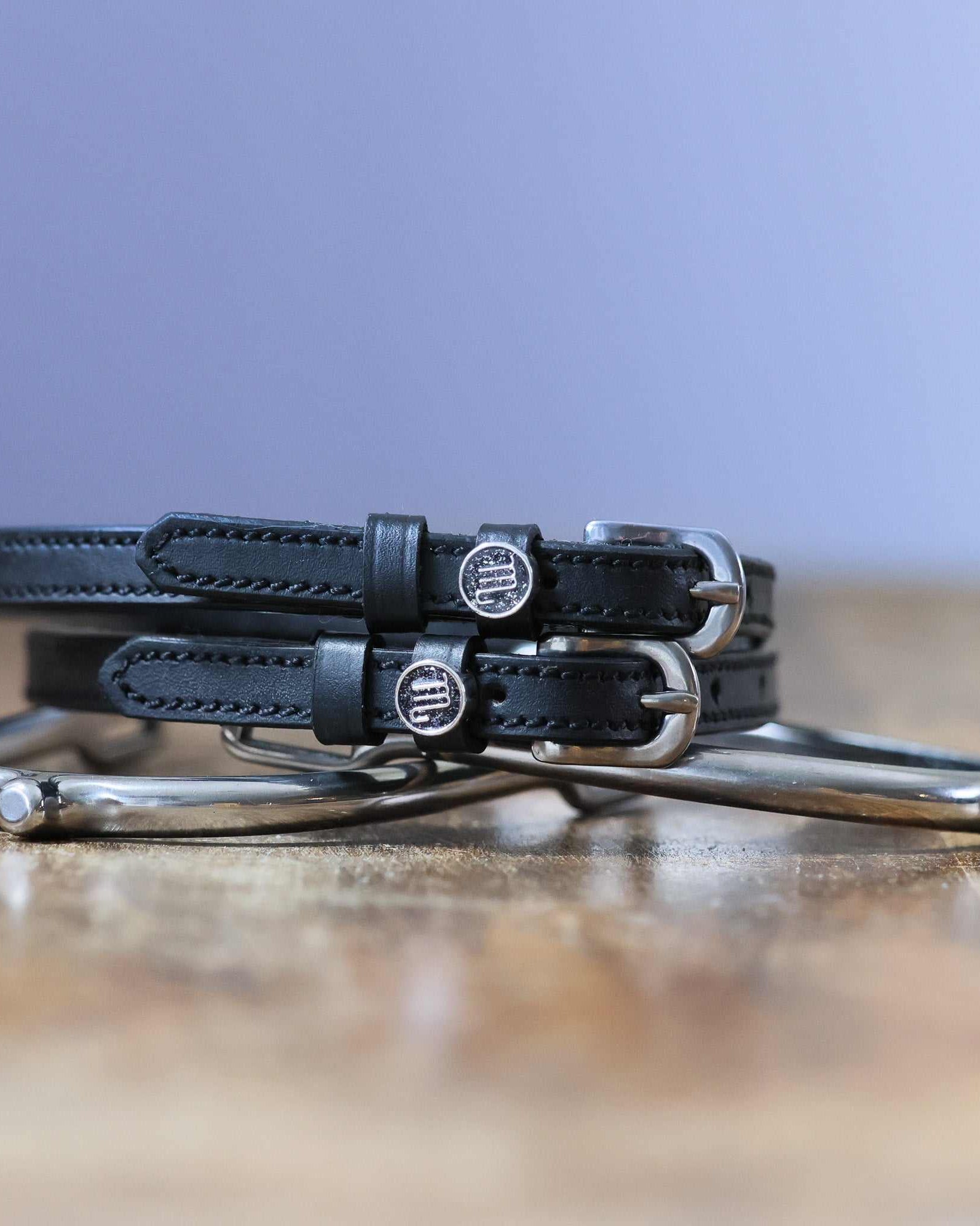 Black leather Scorpio Spur Straps with stainless steel buckles and custom charms on wooden surface
