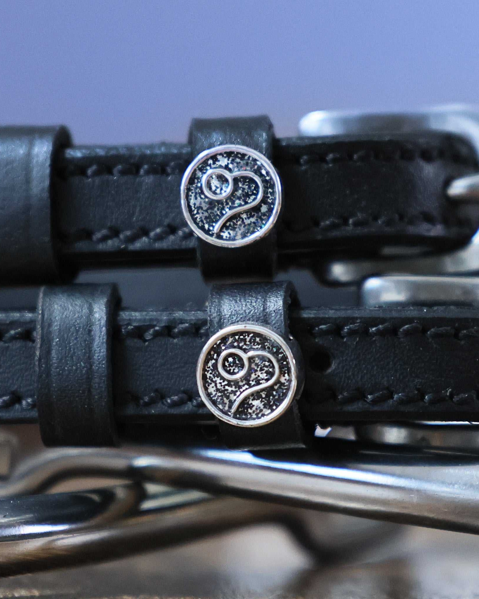 Close-up of black leather Leo Spur Straps with stainless steel buckles and custom Leo zodiac charm