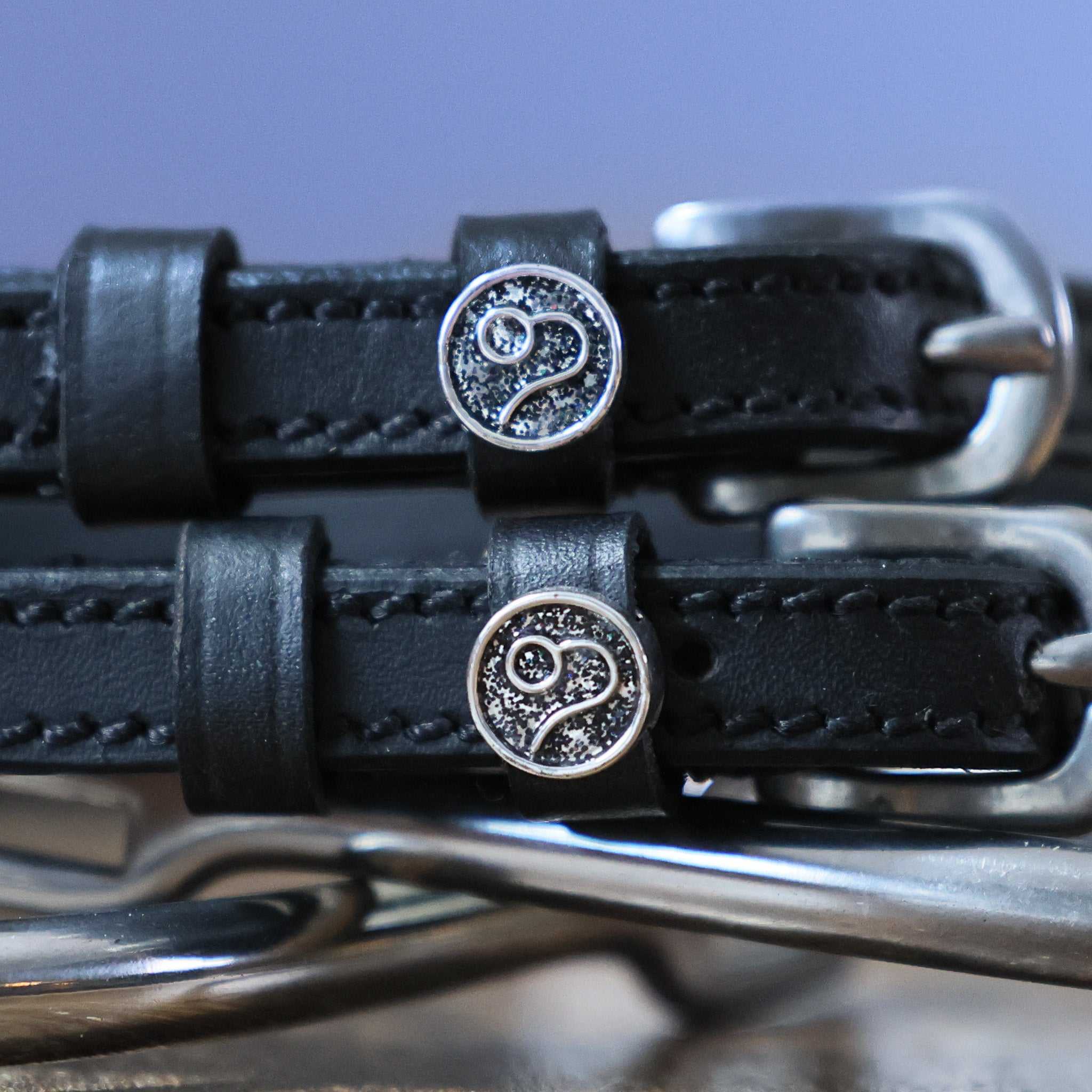 Close-up of black leather Leo Spur Straps with stainless steel buckles and custom Leo zodiac charm