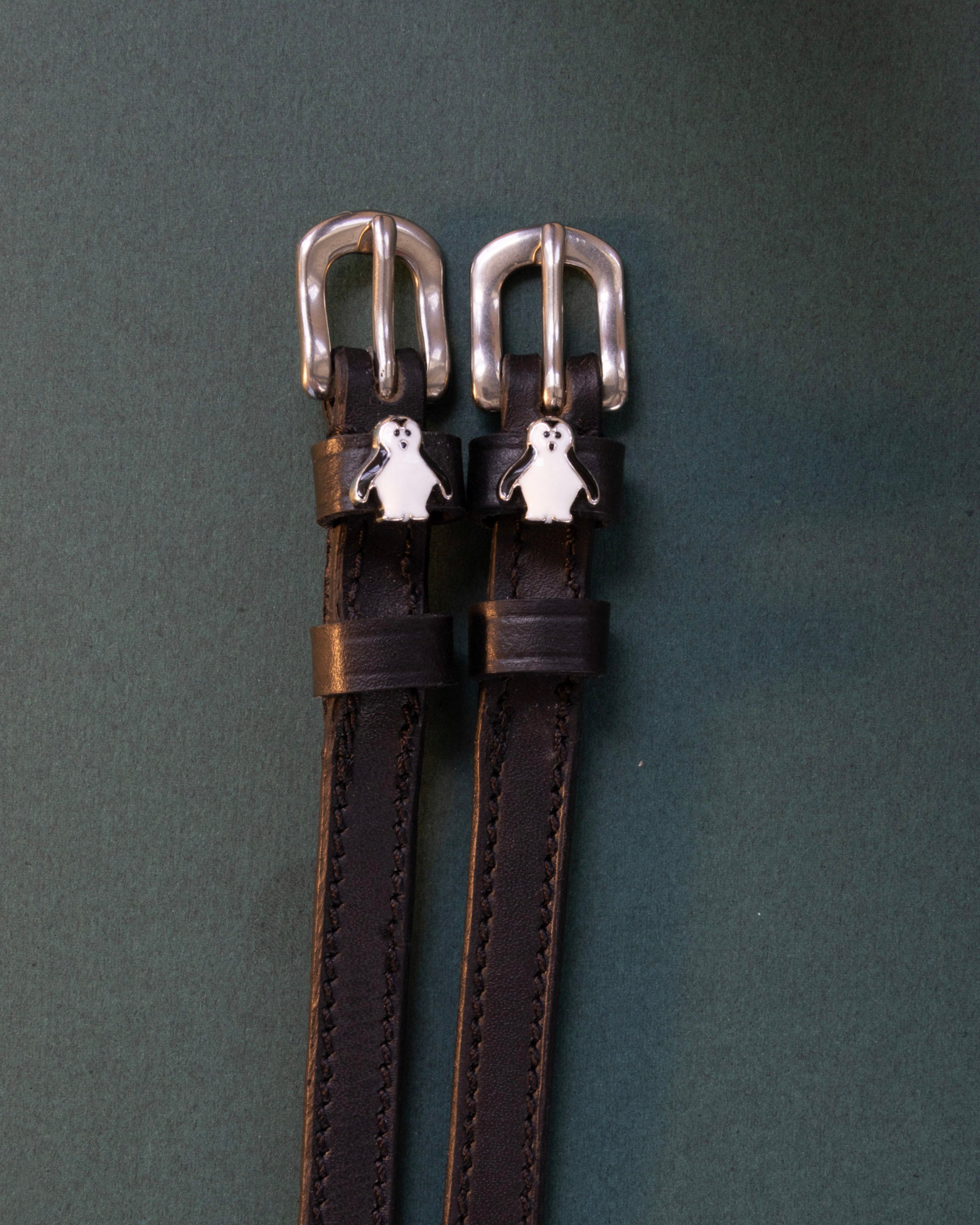 Penguin ManeJane spur straps with the signature Penguin charm, shown on a charcoal background