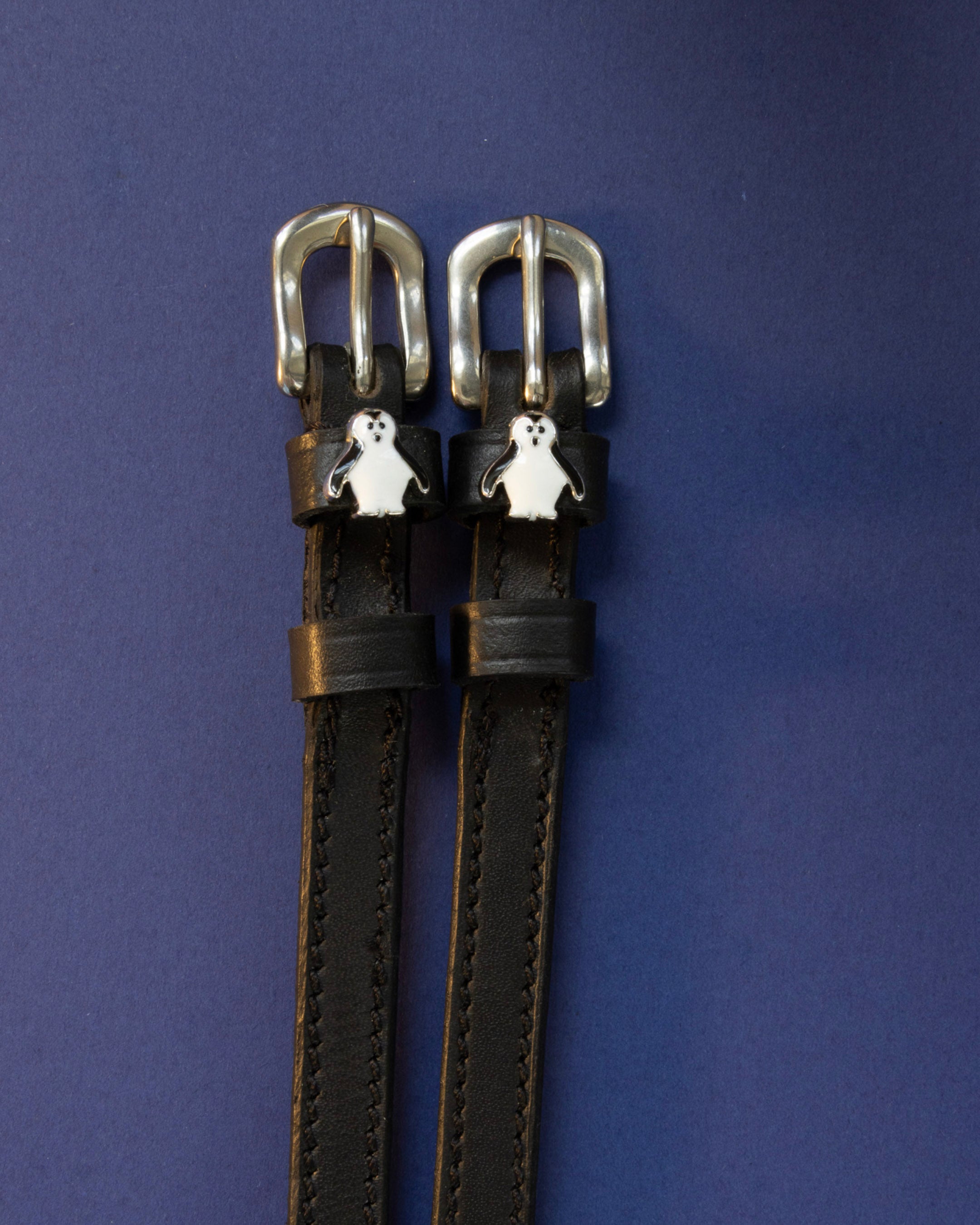 Penguin ManeJane spur straps with the signature Penguin charm, shown on a navy background
