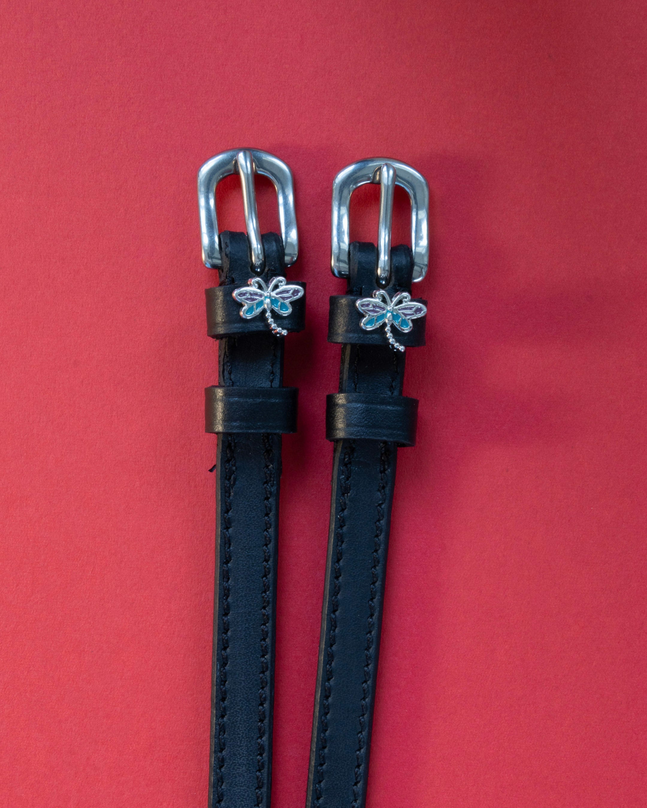 Dragonfly ManeJane spur straps with the signature Dragonfly charm, shown on a red background