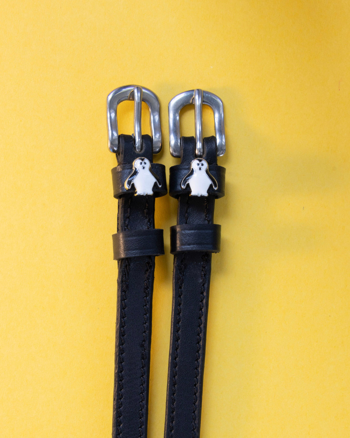 Penguin ManeJane spur straps with the signature Penguin charm, shown on a yellow background