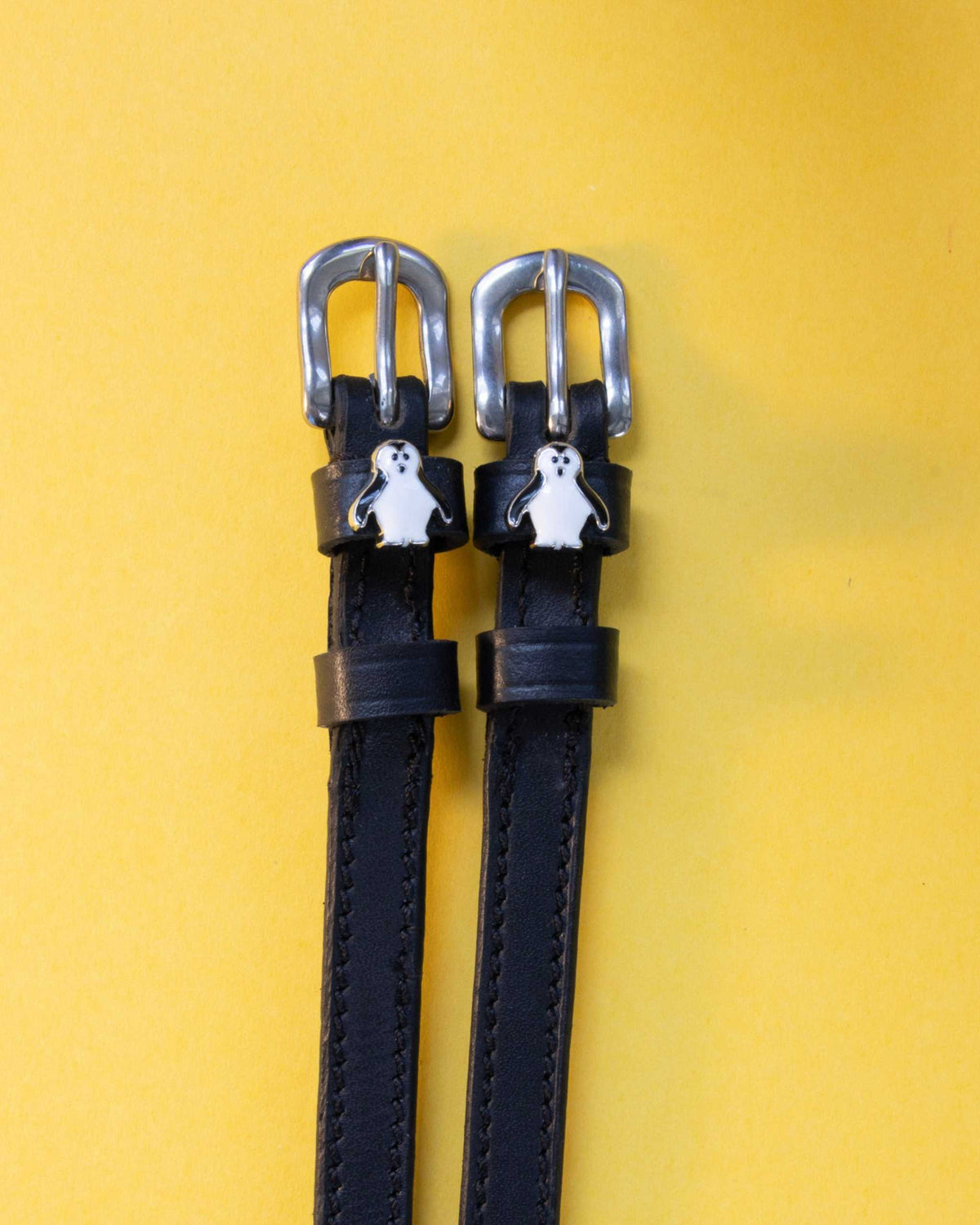 Penguin ManeJane spur straps with the signature Penguin charm, shown on a yellow background