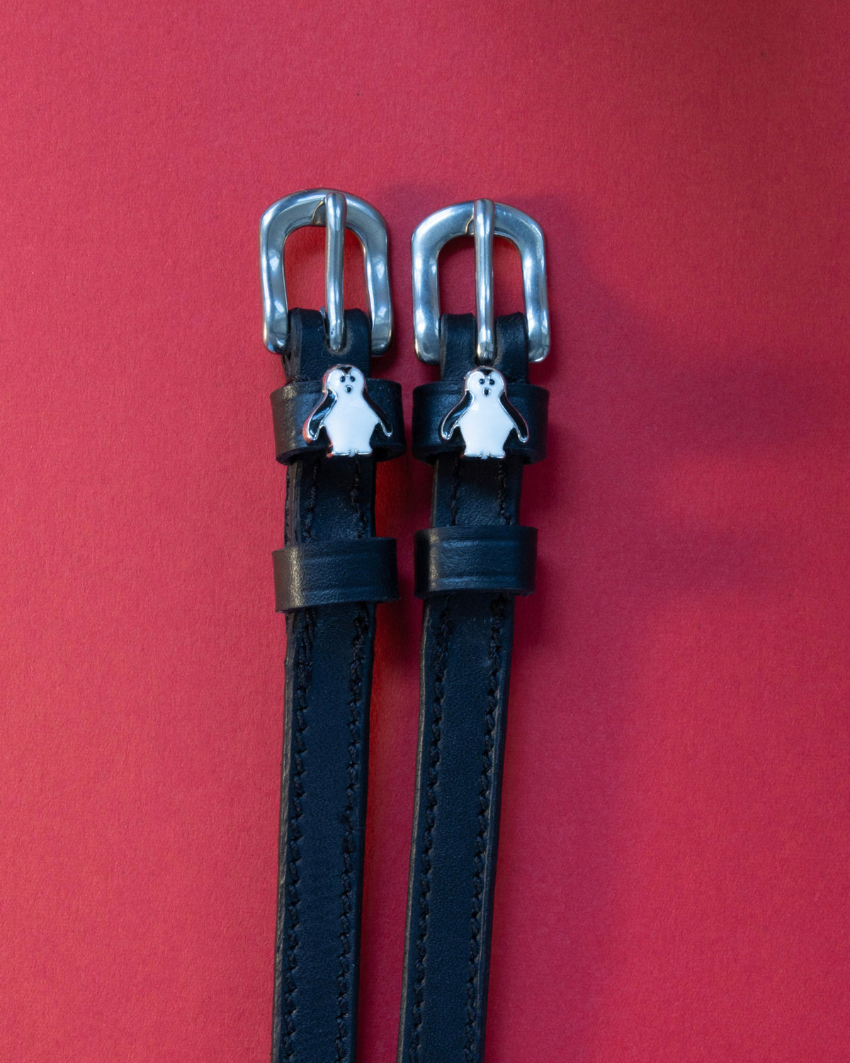 Penguin ManeJane spur straps with the signature Penguin charm, shown on a red background