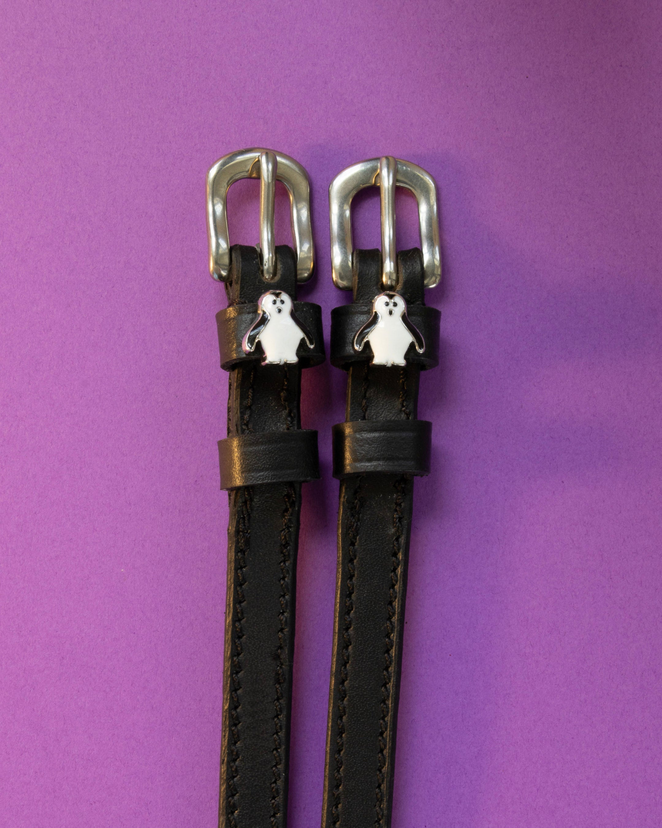 Penguin ManeJane spur straps with the signature Penguin charm, shown on a purple background