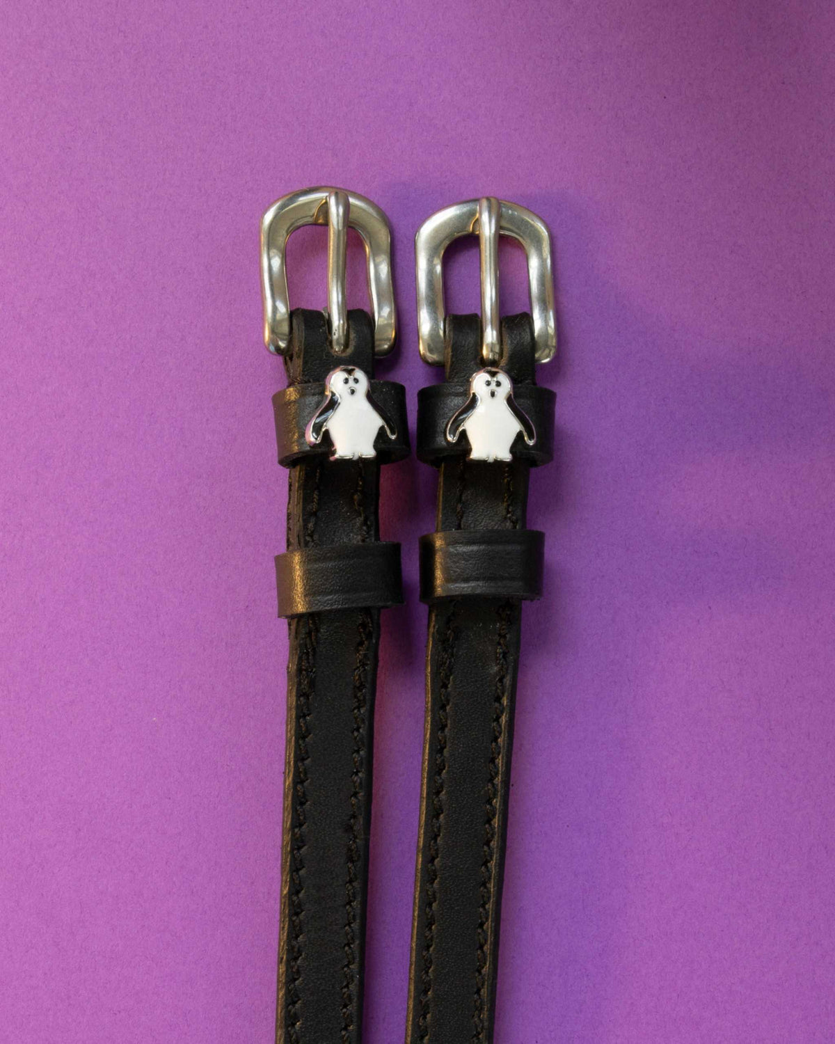 Penguin ManeJane spur straps with the signature Penguin charm, shown on a purple background
