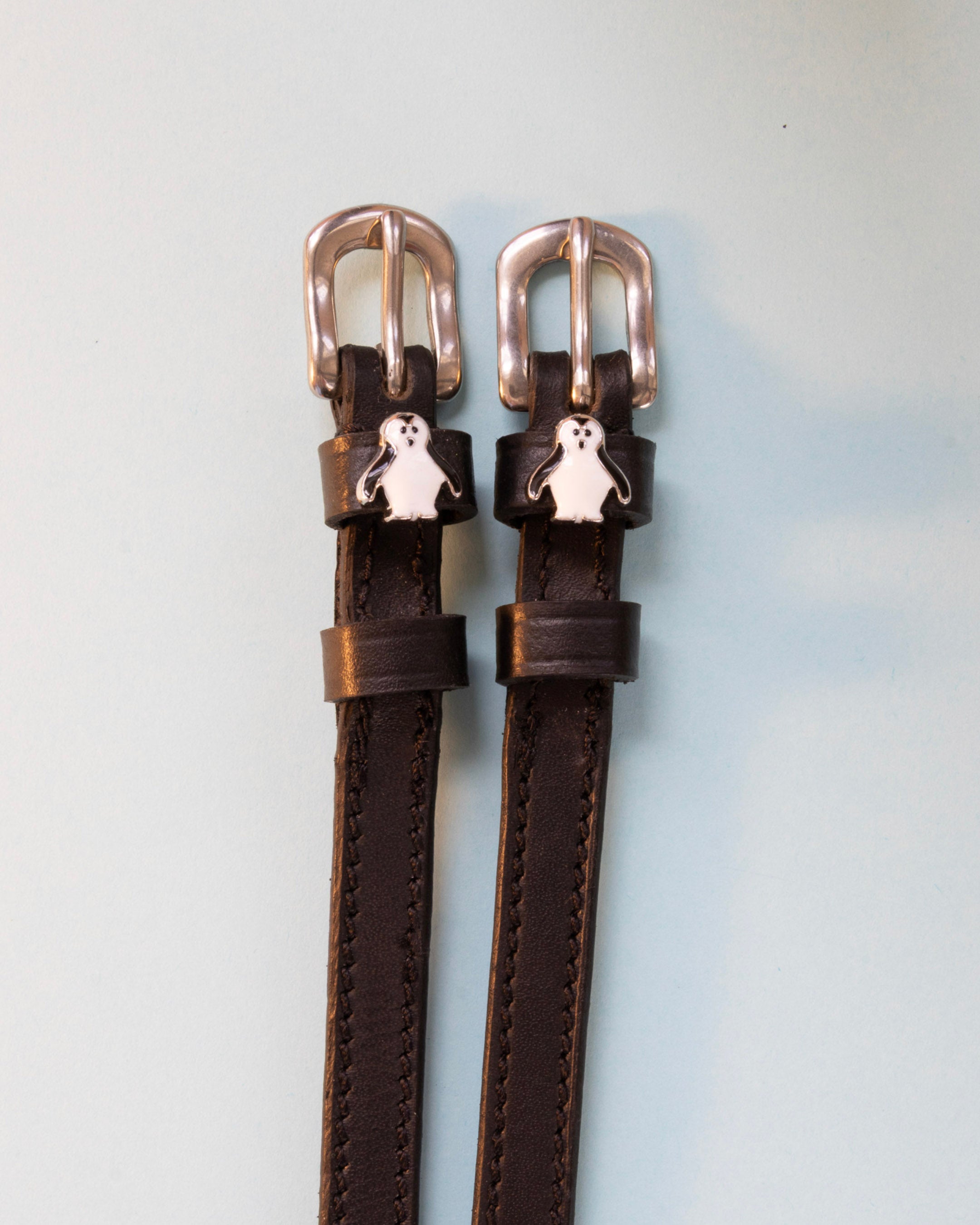 Penguin ManeJane spur straps with the signature Penguin charm, shown on an off-white background
