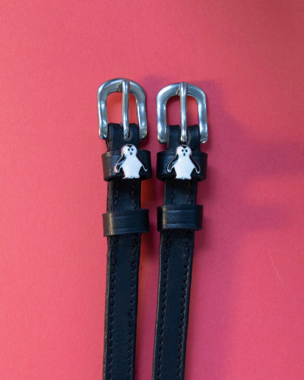 Penguin ManeJane spur straps with the signature Penguin charm, shown on a coral background