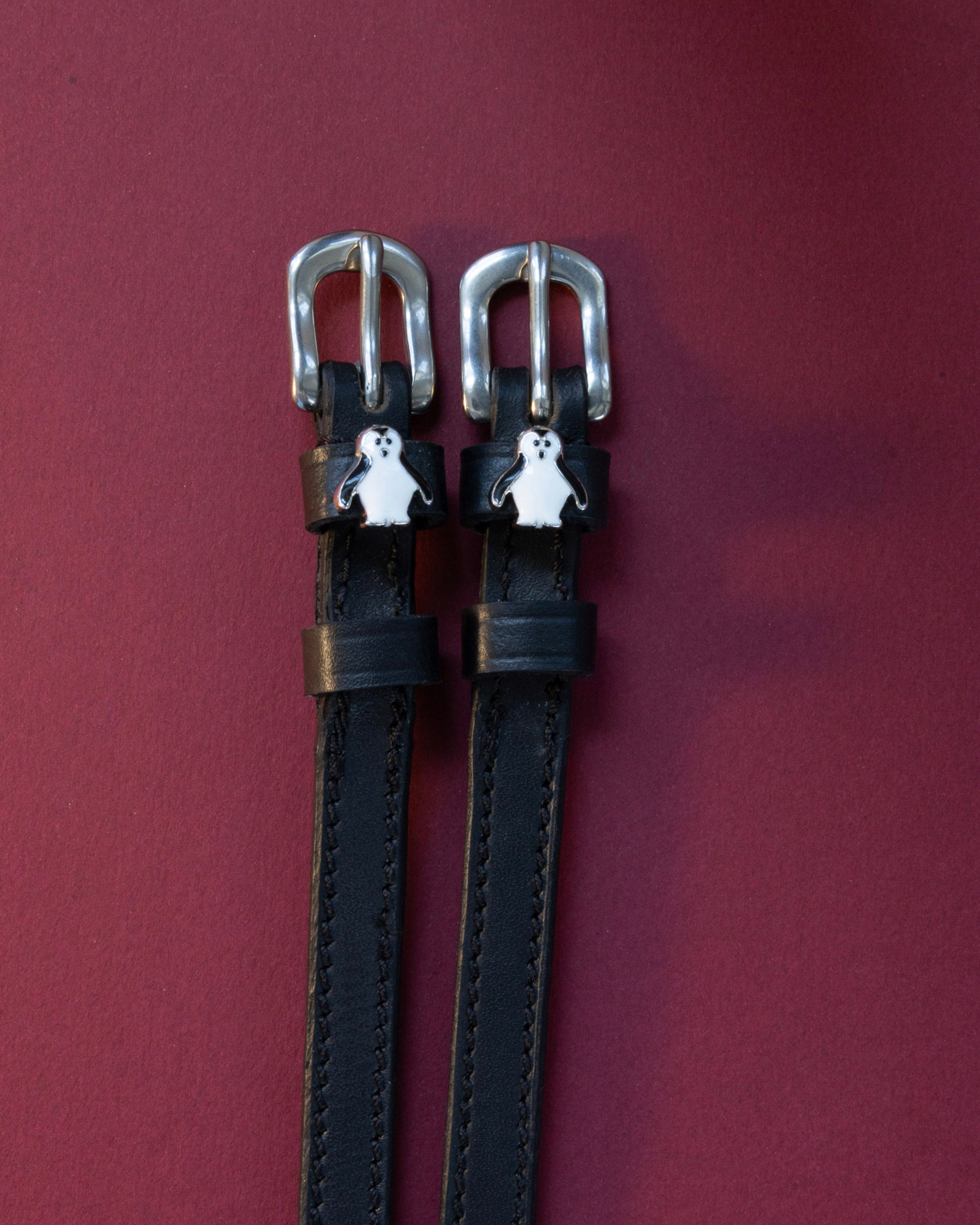 Penguin ManeJane spur straps with the signature Penguin charm, shown on a plum background