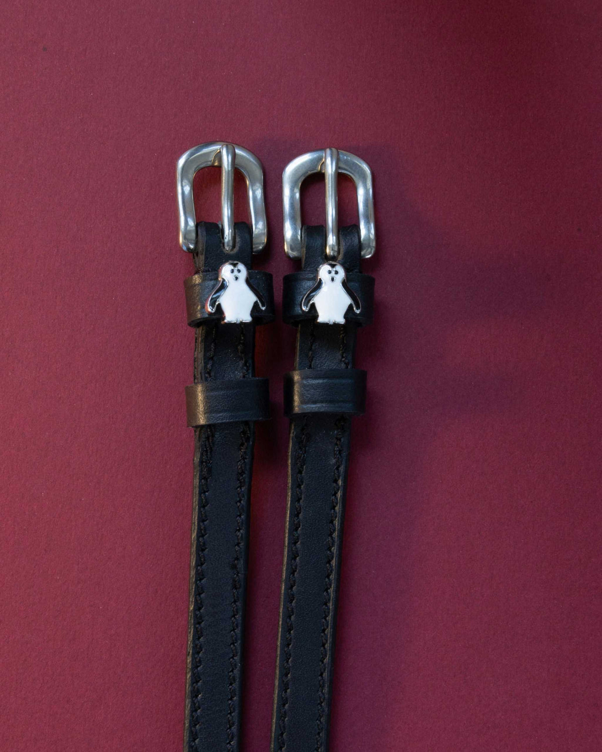 Penguin ManeJane spur straps with the signature Penguin charm, shown on a plum background