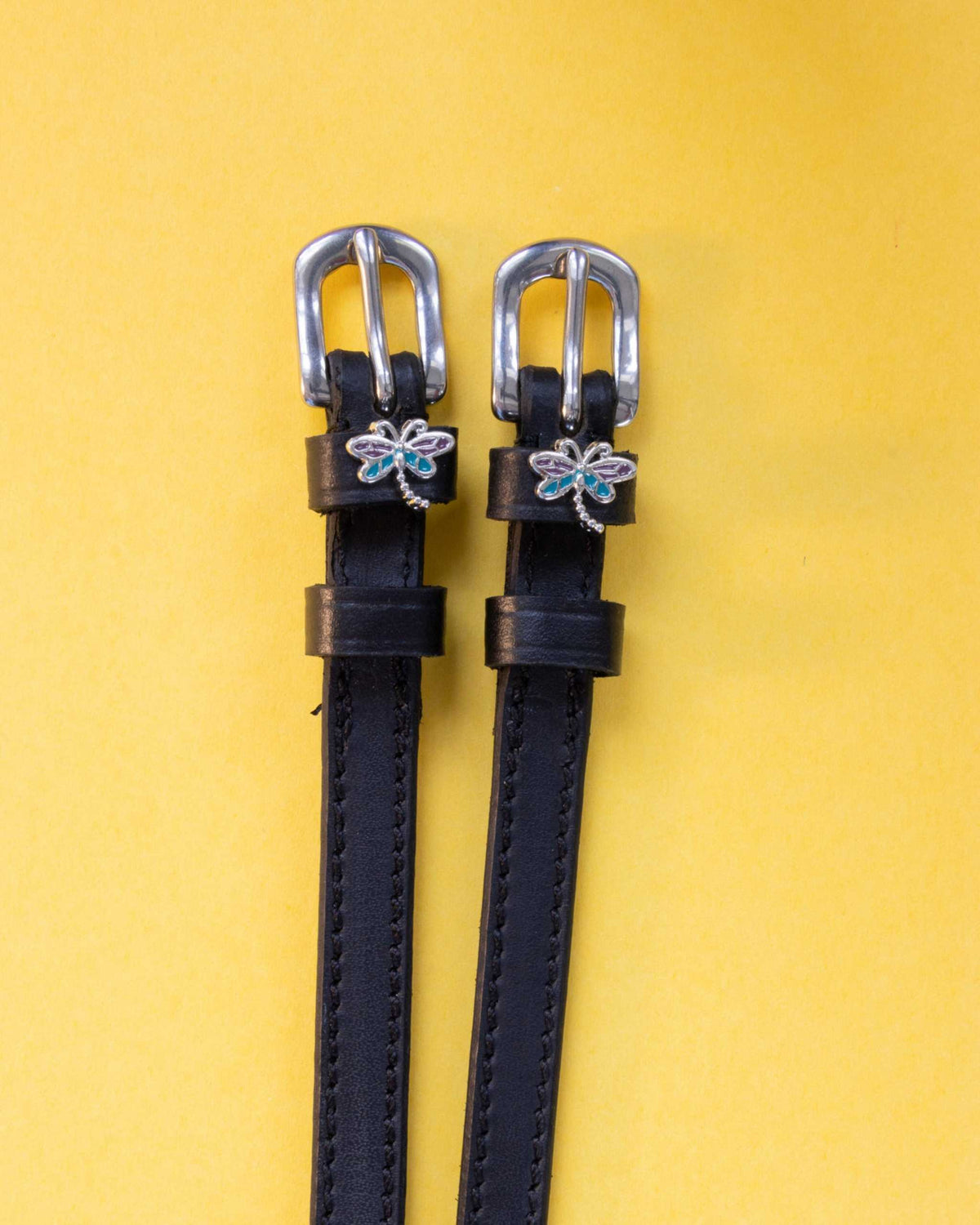 Dragonfly ManeJane spur straps with the signature Dragonfly charm, shown on a yellow background