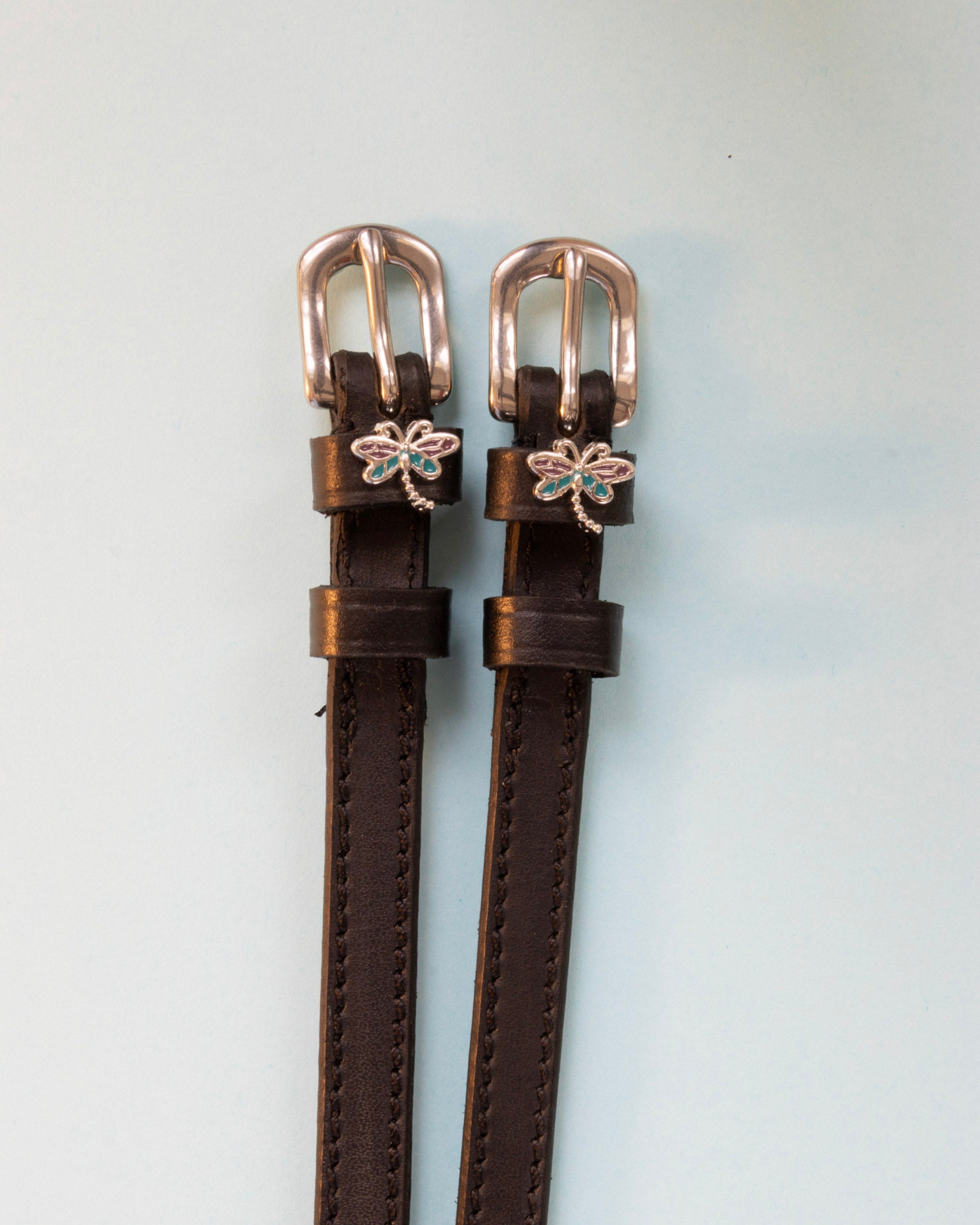 Dragonfly ManeJane spur straps with the signature Dragonfly charm, shown on an off-white background
