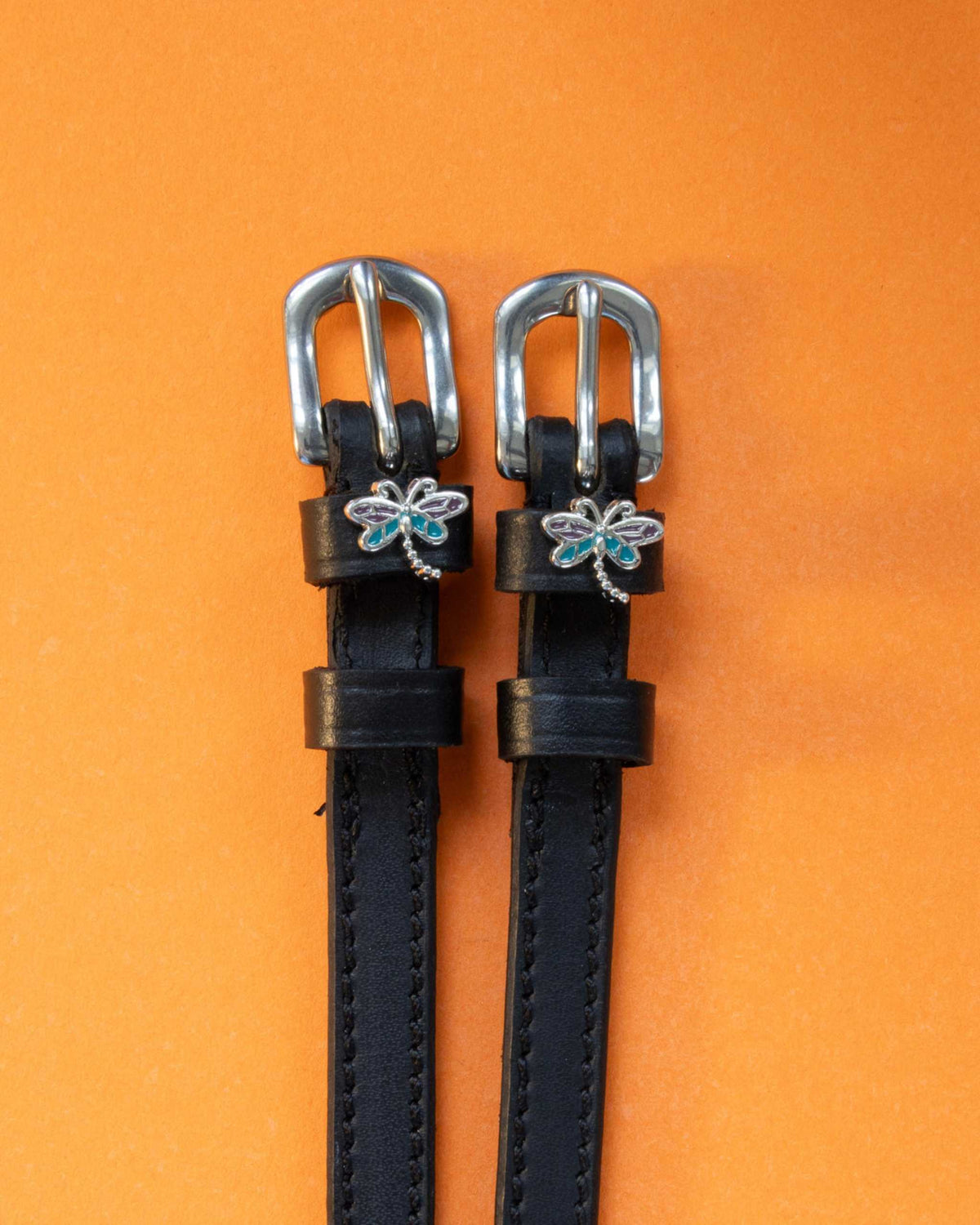 Dragonfly ManeJane spur straps with the signature Dragonfly charm, shown on an orange background