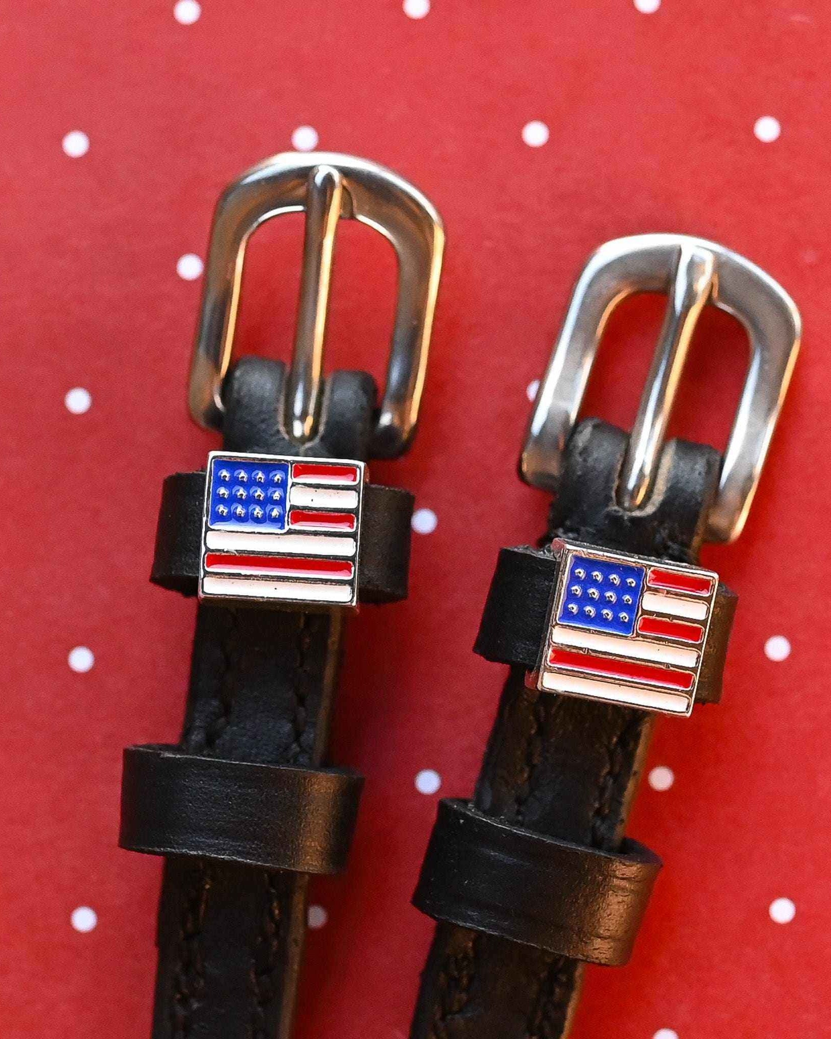 American flag charms and silver buckles on black spur straps, red polka-dot backdrop