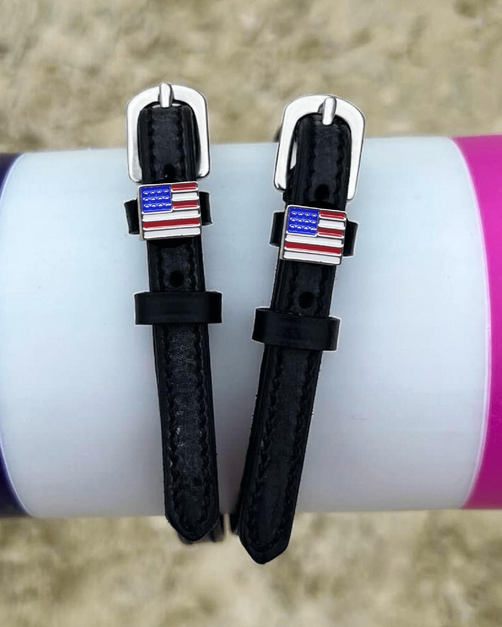 Black leather American flag spur straps draped over a colorful jump pole