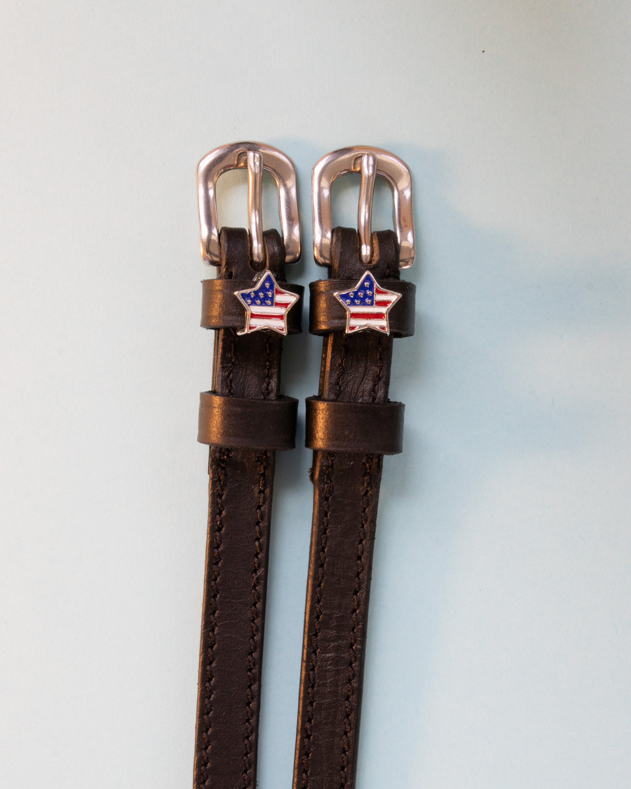 Brown leather American-flag star spur straps with rose-gold buckles, flat-lay