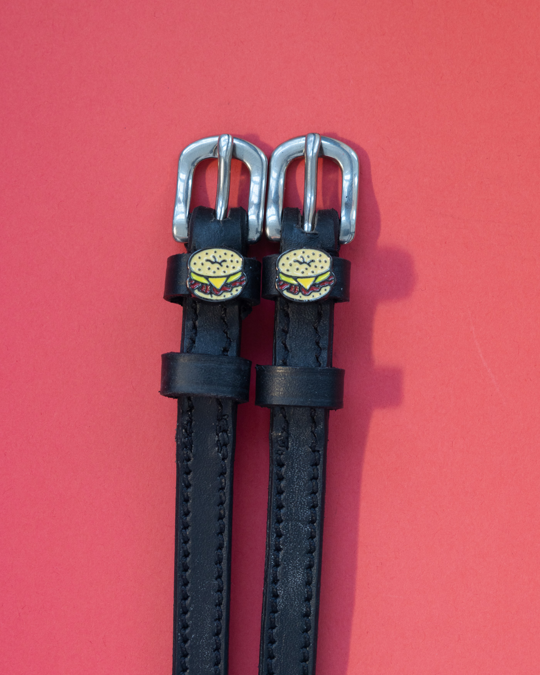 Pair of black leather ManeJane spur straps with bagel sandwich charms on pink