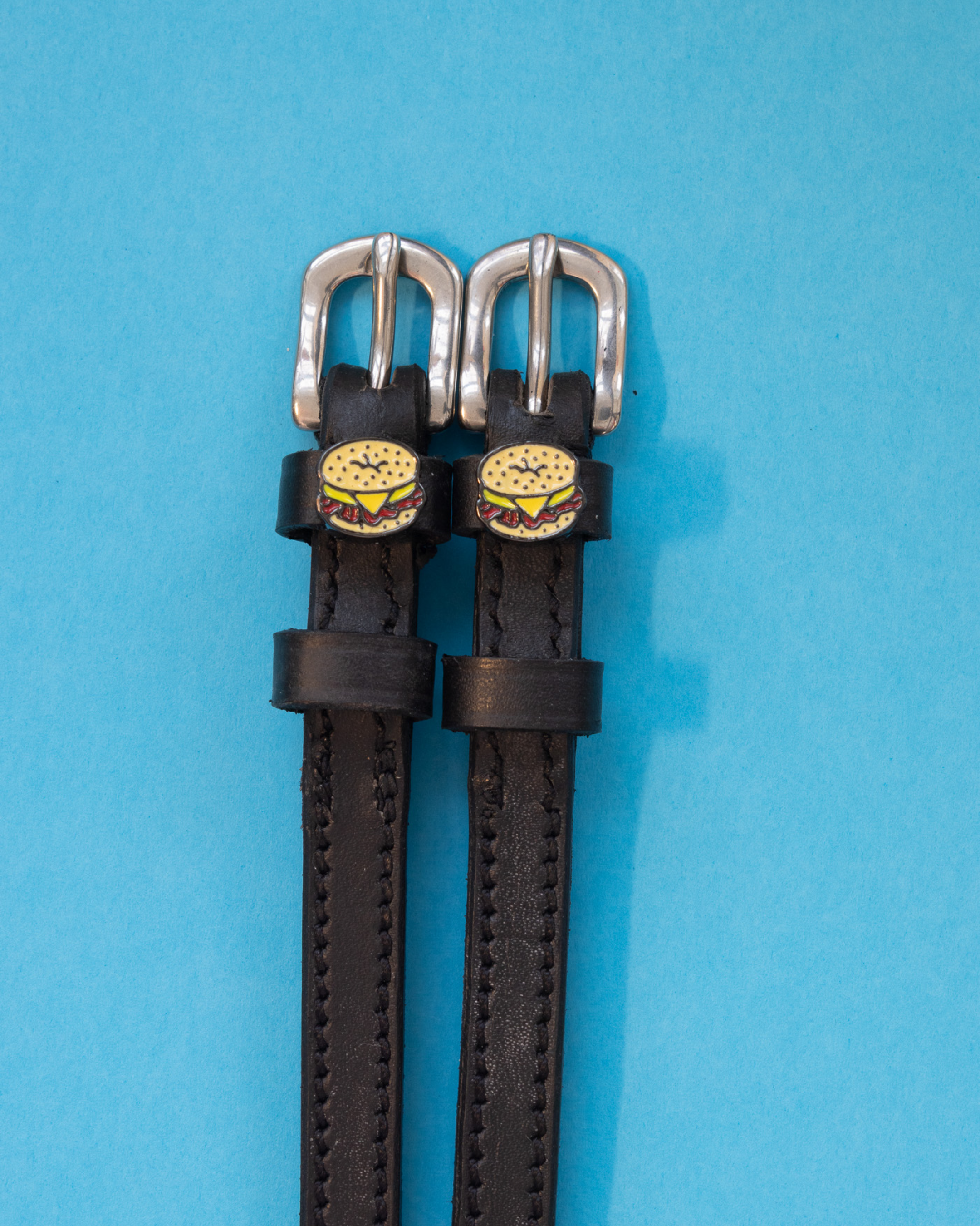 Black leather bagel sandwich spur straps flat-laid on a blue background