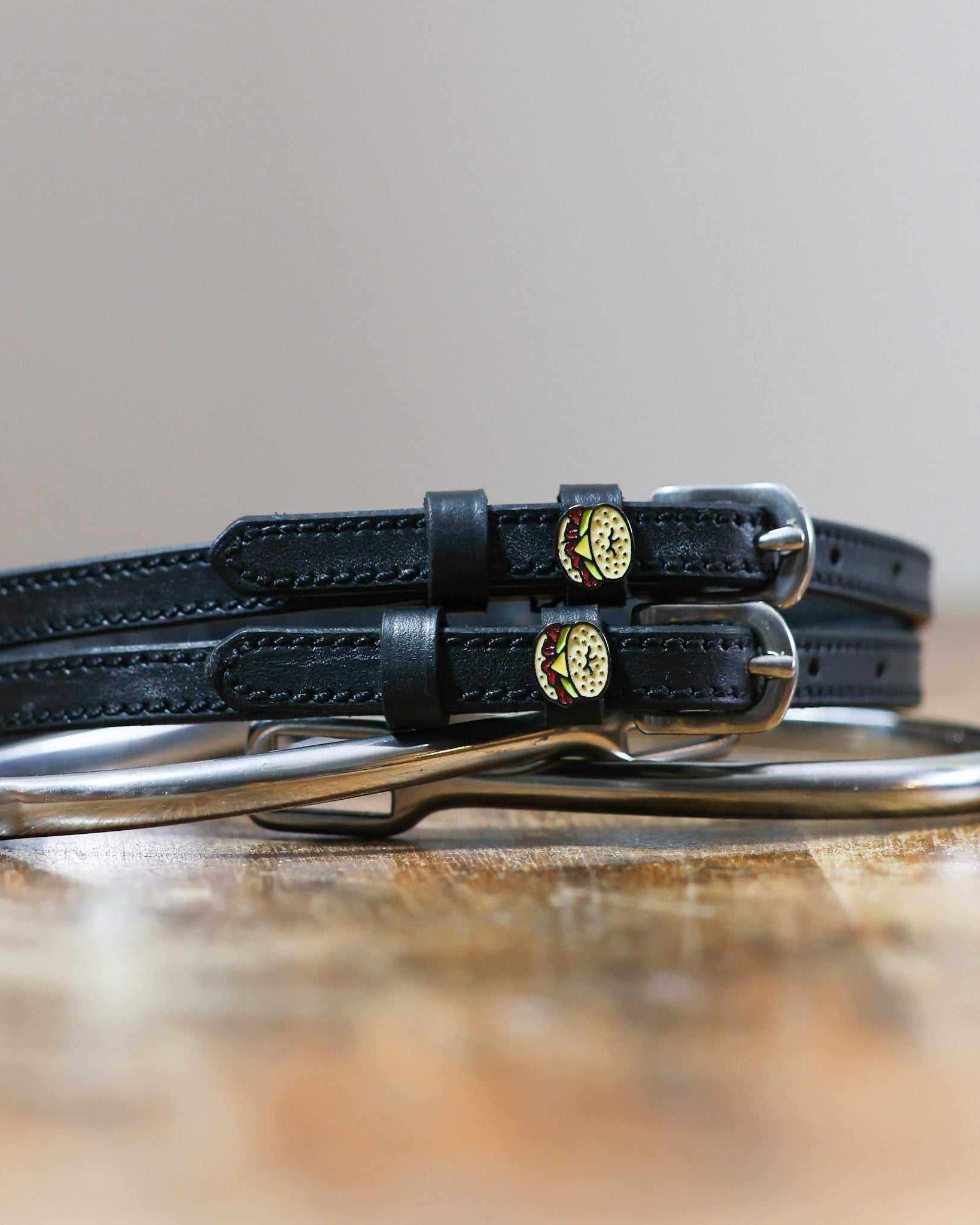 Black leather bagel sandwich spur straps coiled beside a spur on wood