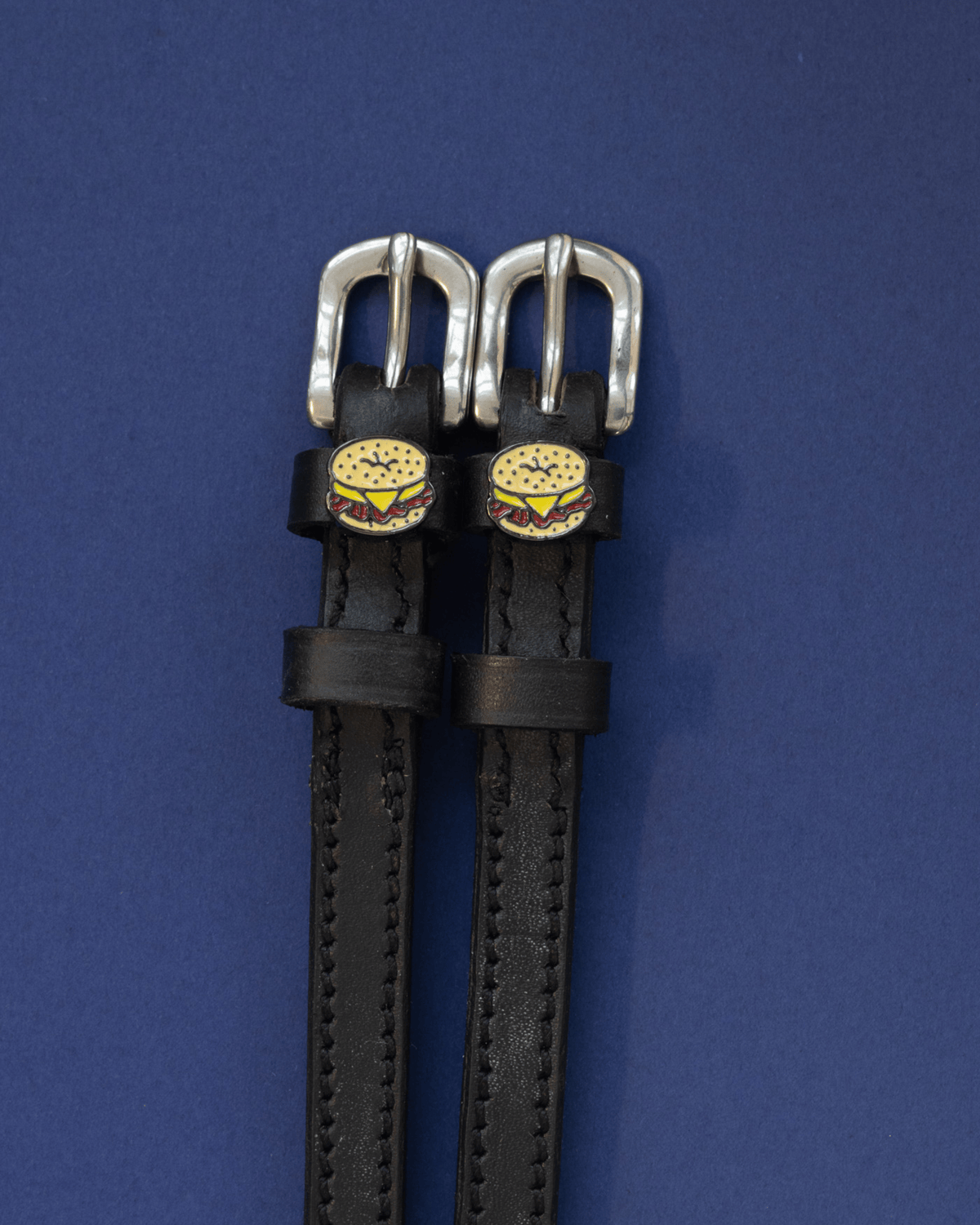 Pair of black leather bagel sandwich spur straps on a navy background