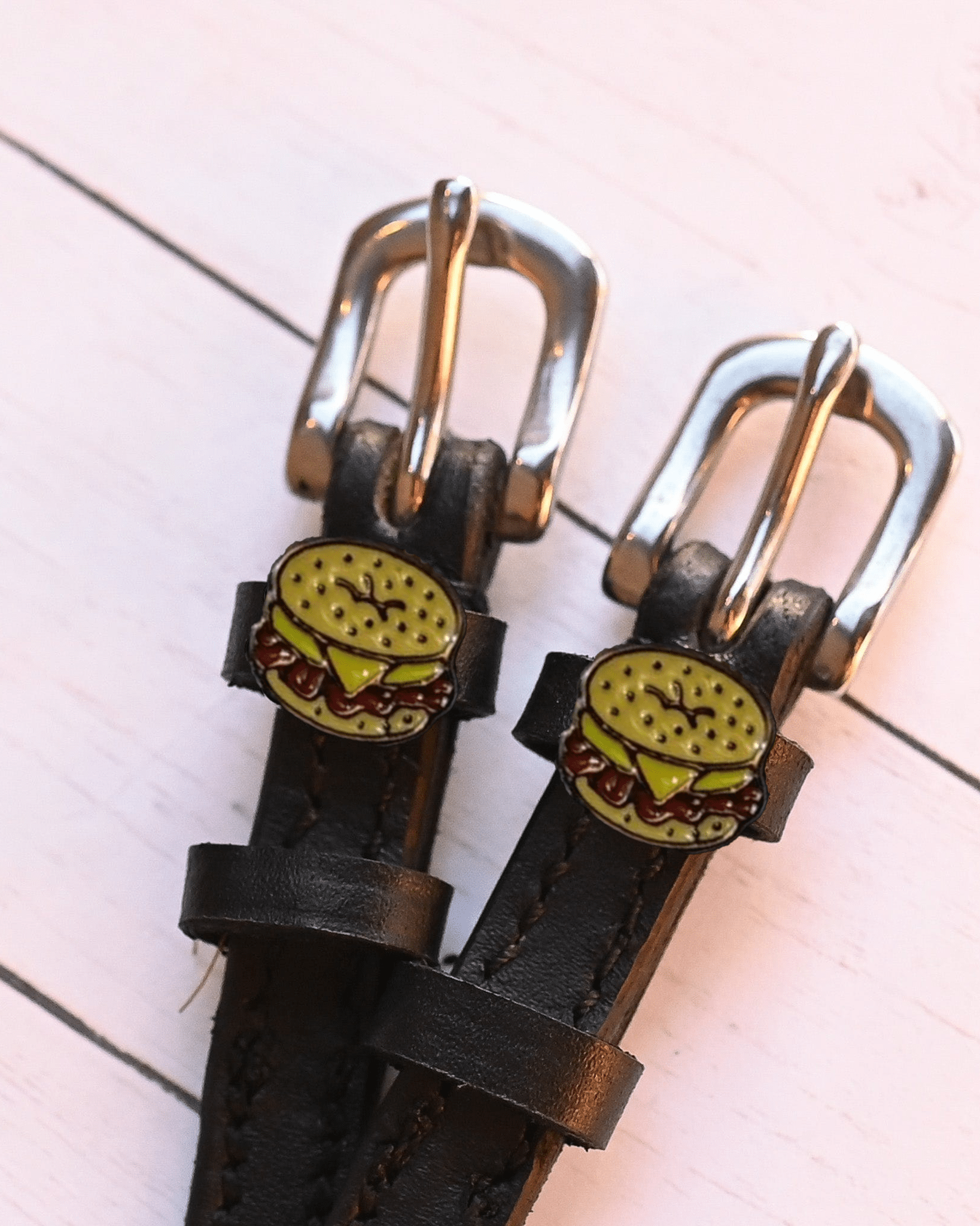 Two bagel sandwich charms on black leather spur straps over pink planks