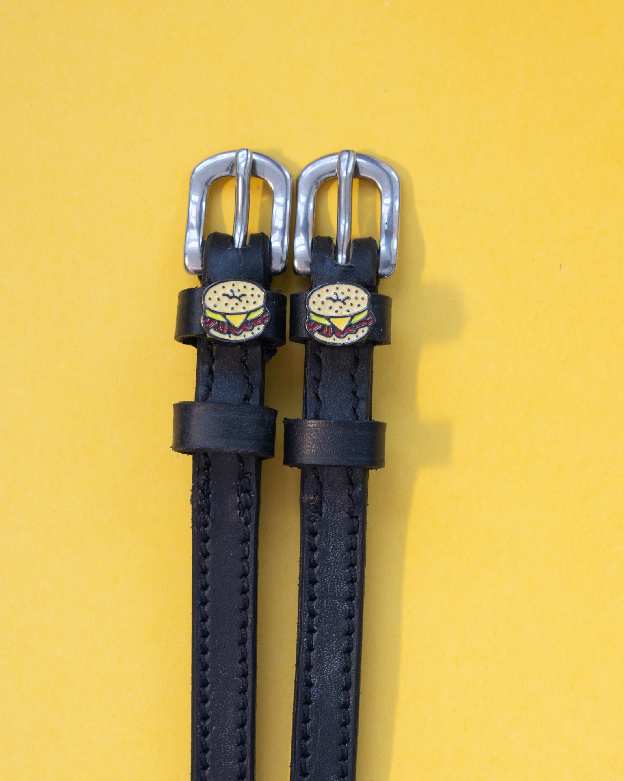Black leather bagel sandwich spur straps on a yellow background