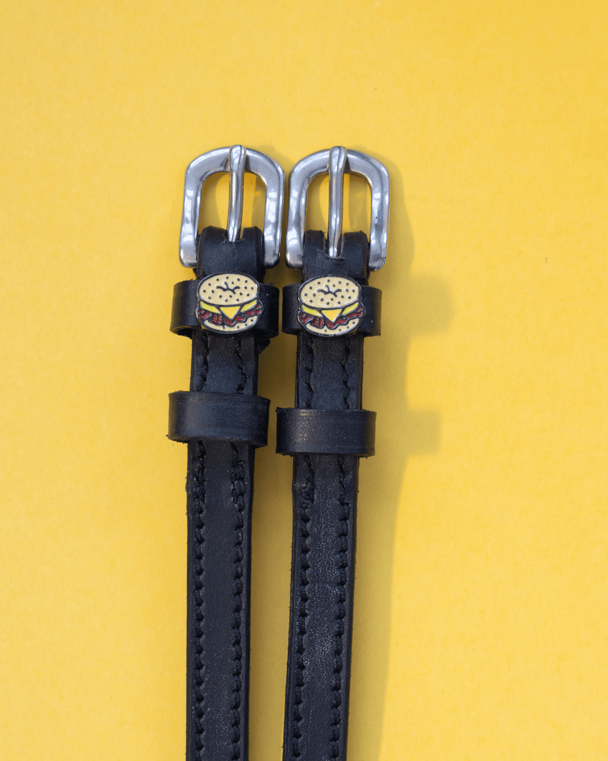 Black leather bagel sandwich spur straps on a yellow background