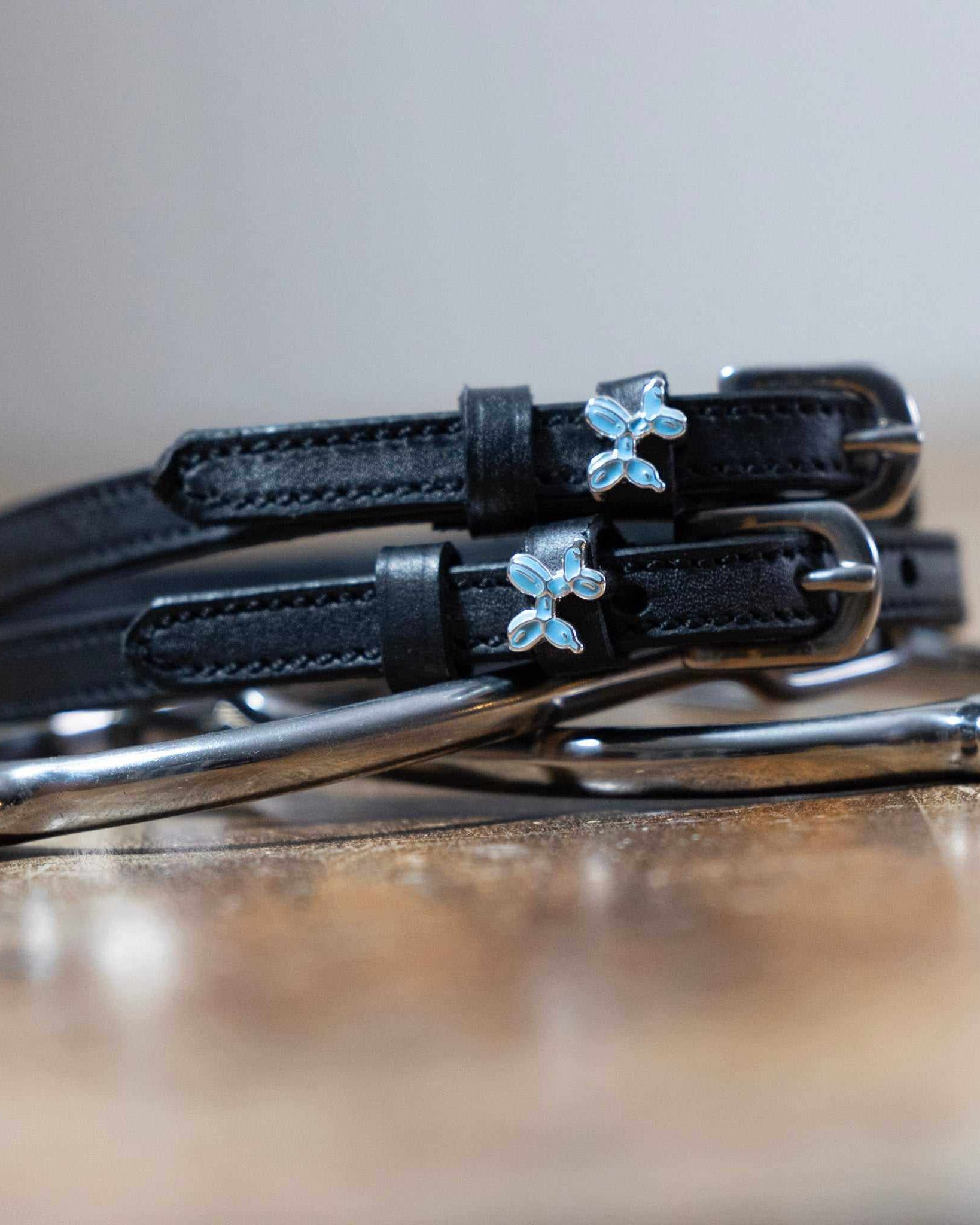 Black leather balloon dog spur straps coiled on wood beside a silver bit