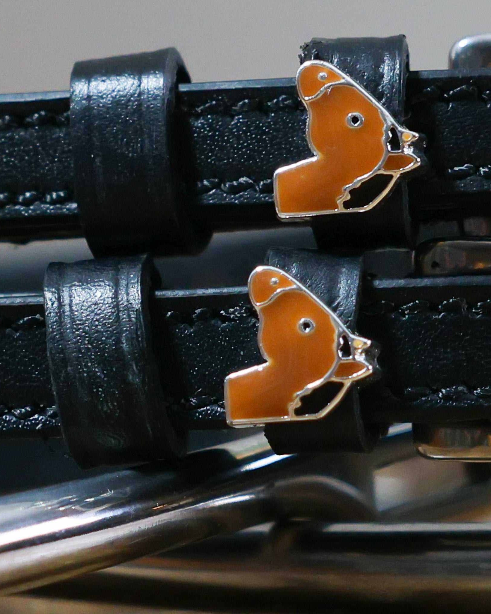 Close-up of tan horse-head charms on black leather ManeJane spur strap keepers