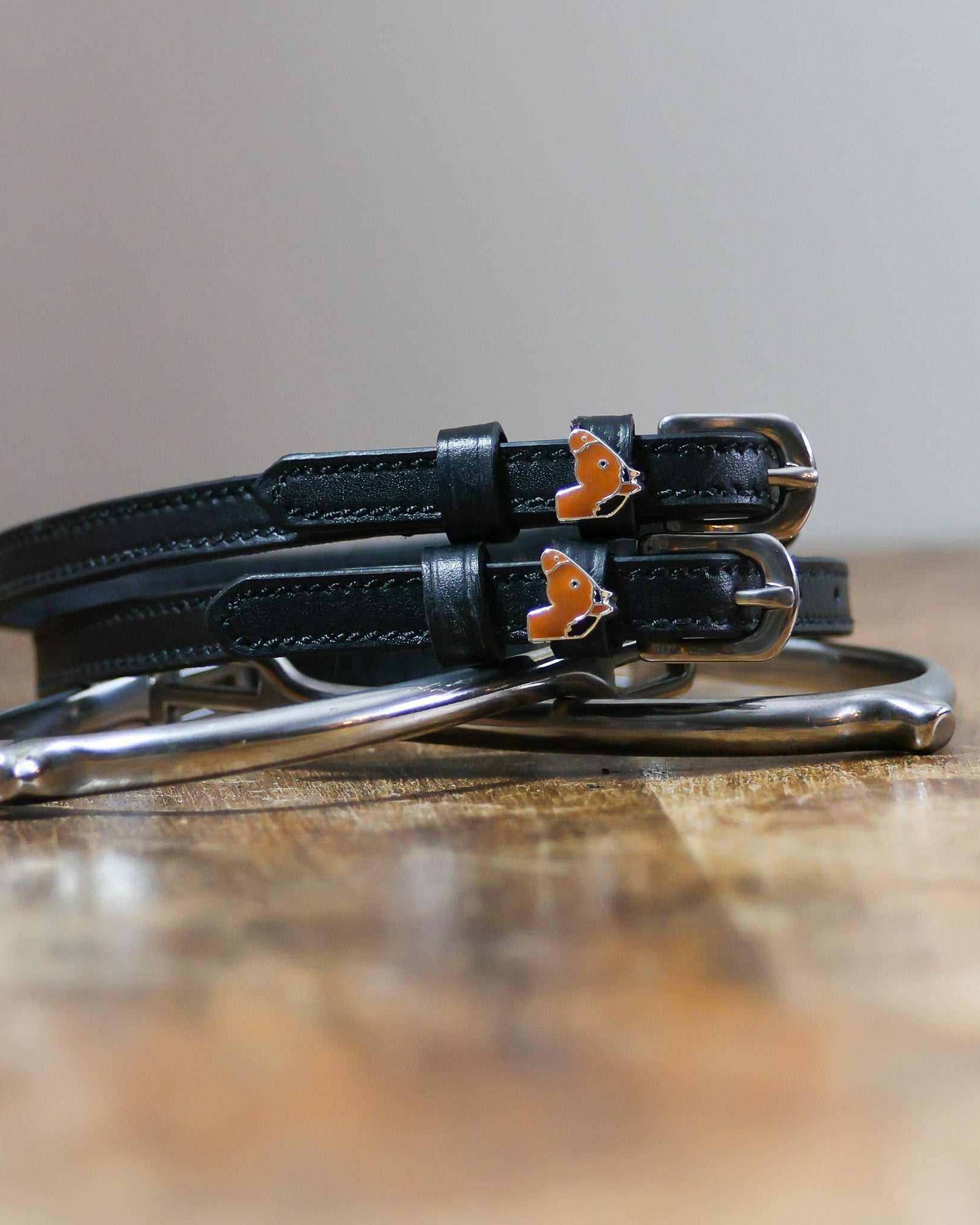 Coiled black leather spur straps and a silver spur on wood with horse-head charms