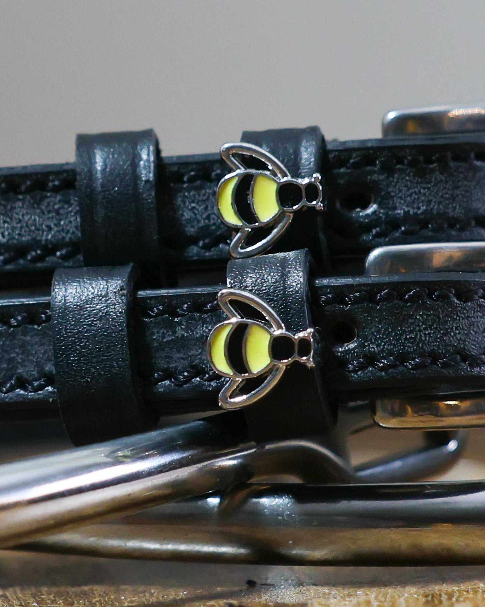 Close-up of silver-and-yellow bee charms on black leather ManeJane spur strap keepers