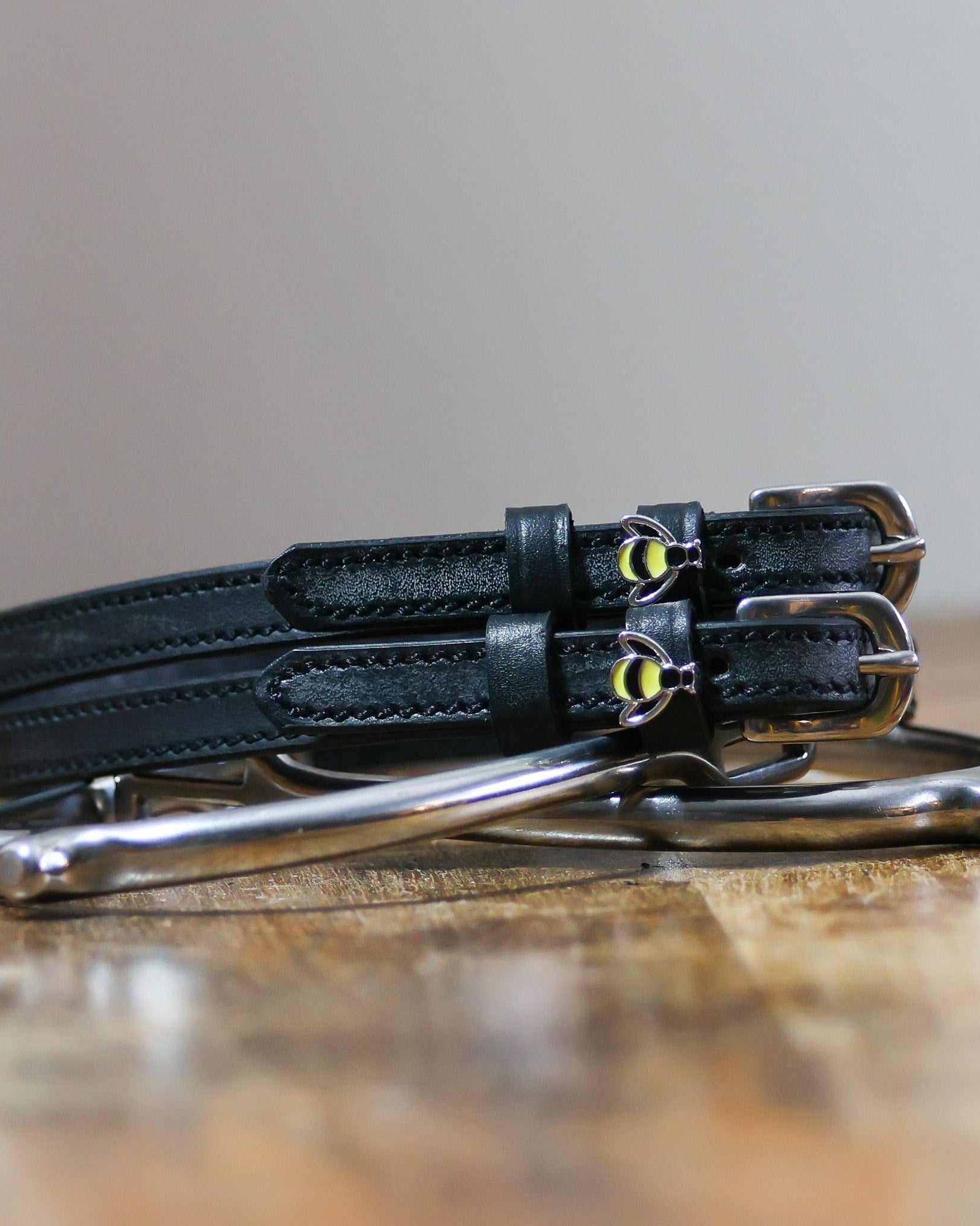 Black bee spur straps coiled on a silver stirrup on a wooden table