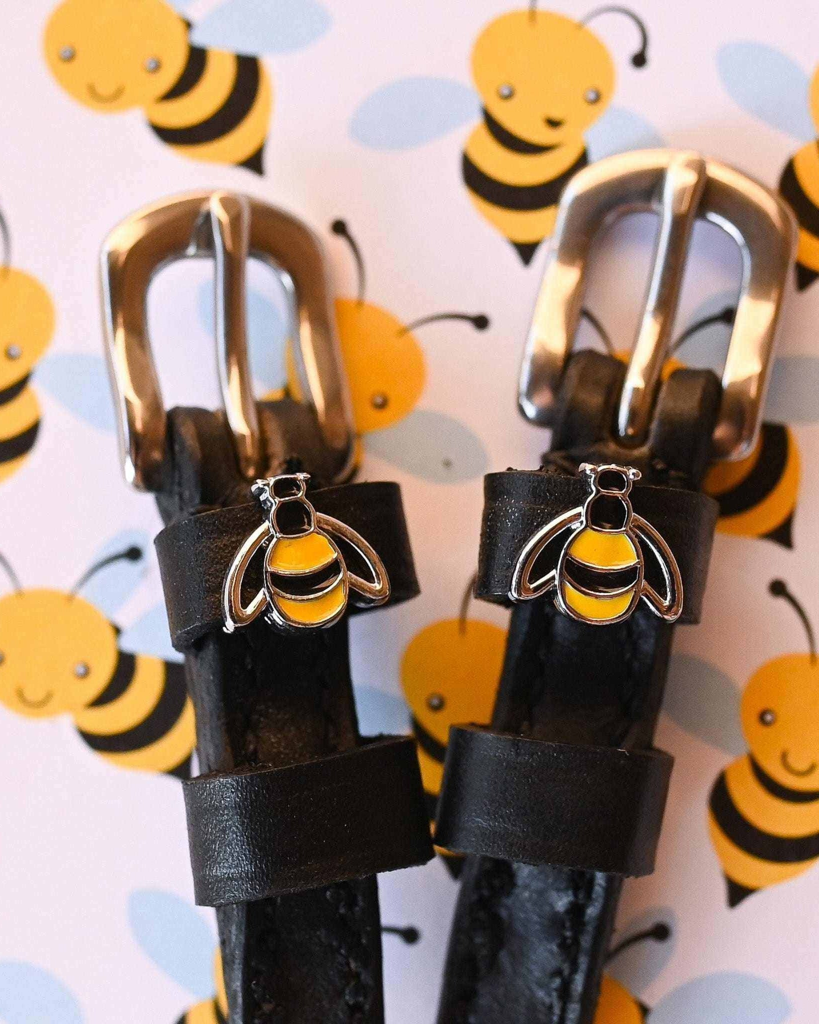 Bumblebee charms on black leather spur straps against a cartoon bee print backdrop