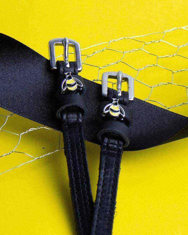 Bee spur straps buckled and fastened, bumblebee charms visible, on a yellow backdrop